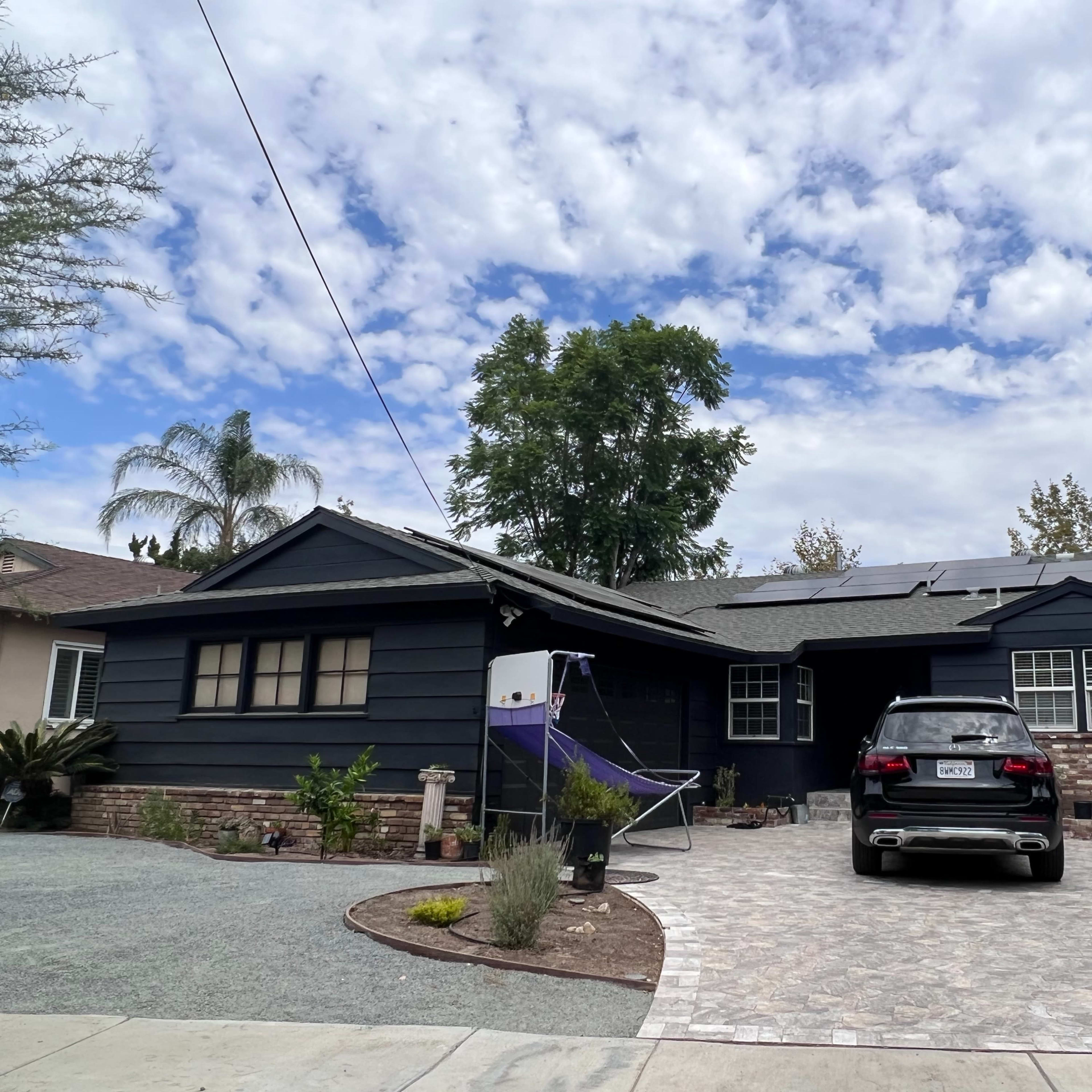 A dark-painted house with solar panels on the roof, a paved driveway, and a car parked in front.