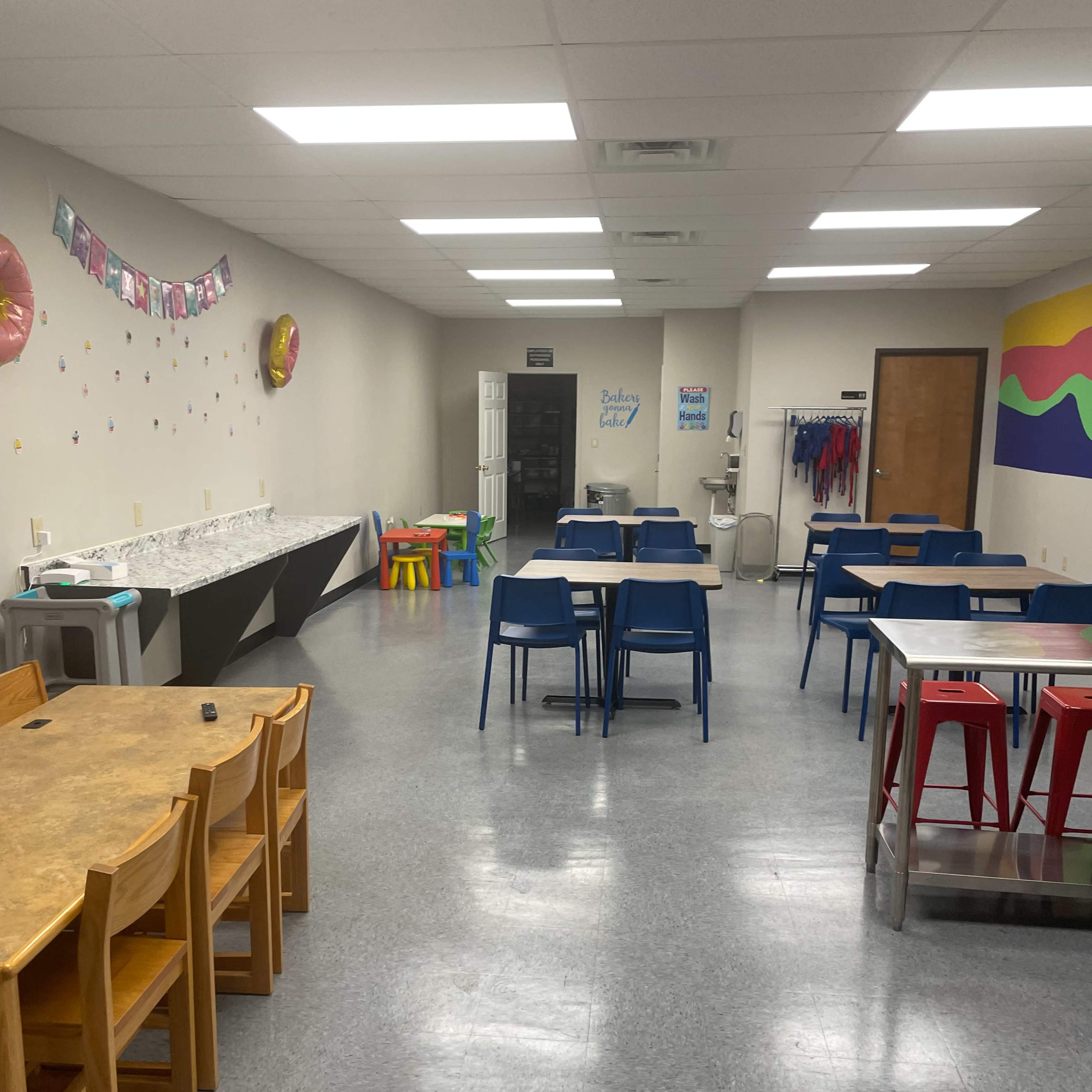 A spacious classroom with several tables and chairs arranged neatly, along with colorful wall decorations and a water cooler.
