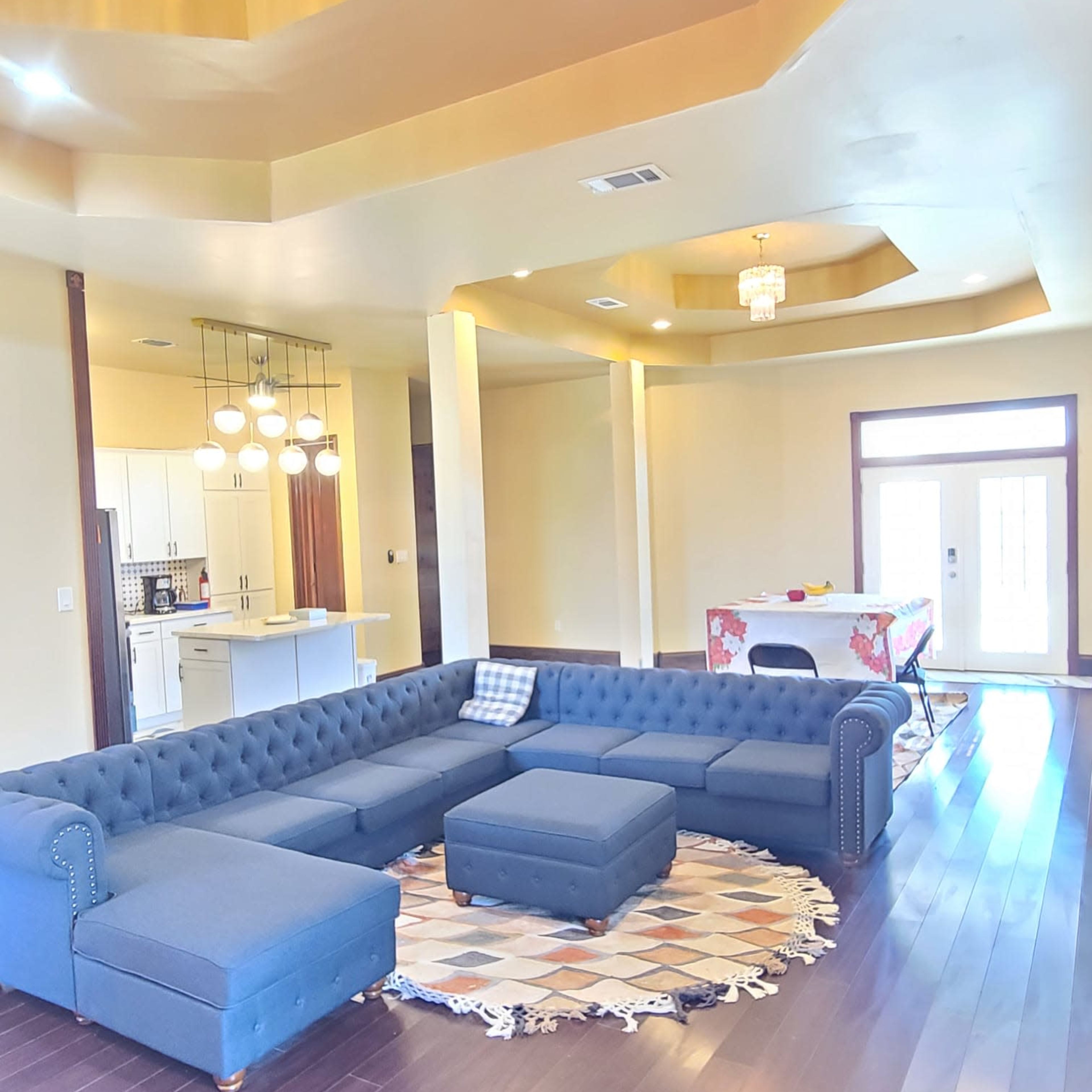 A spacious living room with a navy blue sectional sofa, a round patterned rug, and a modern dining area in the background.