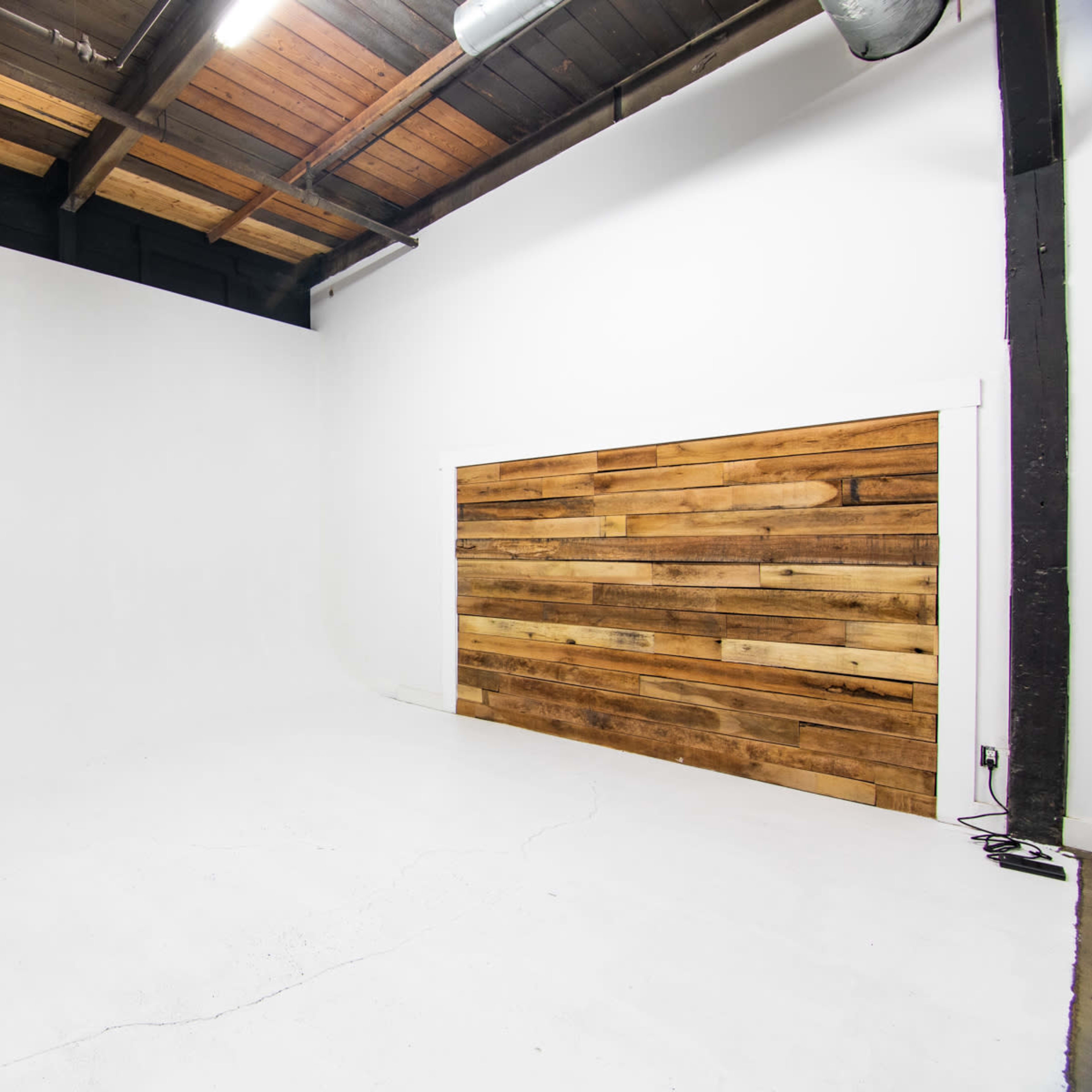 An empty photography studio with a smooth white backdrop and a wooden accent wall.