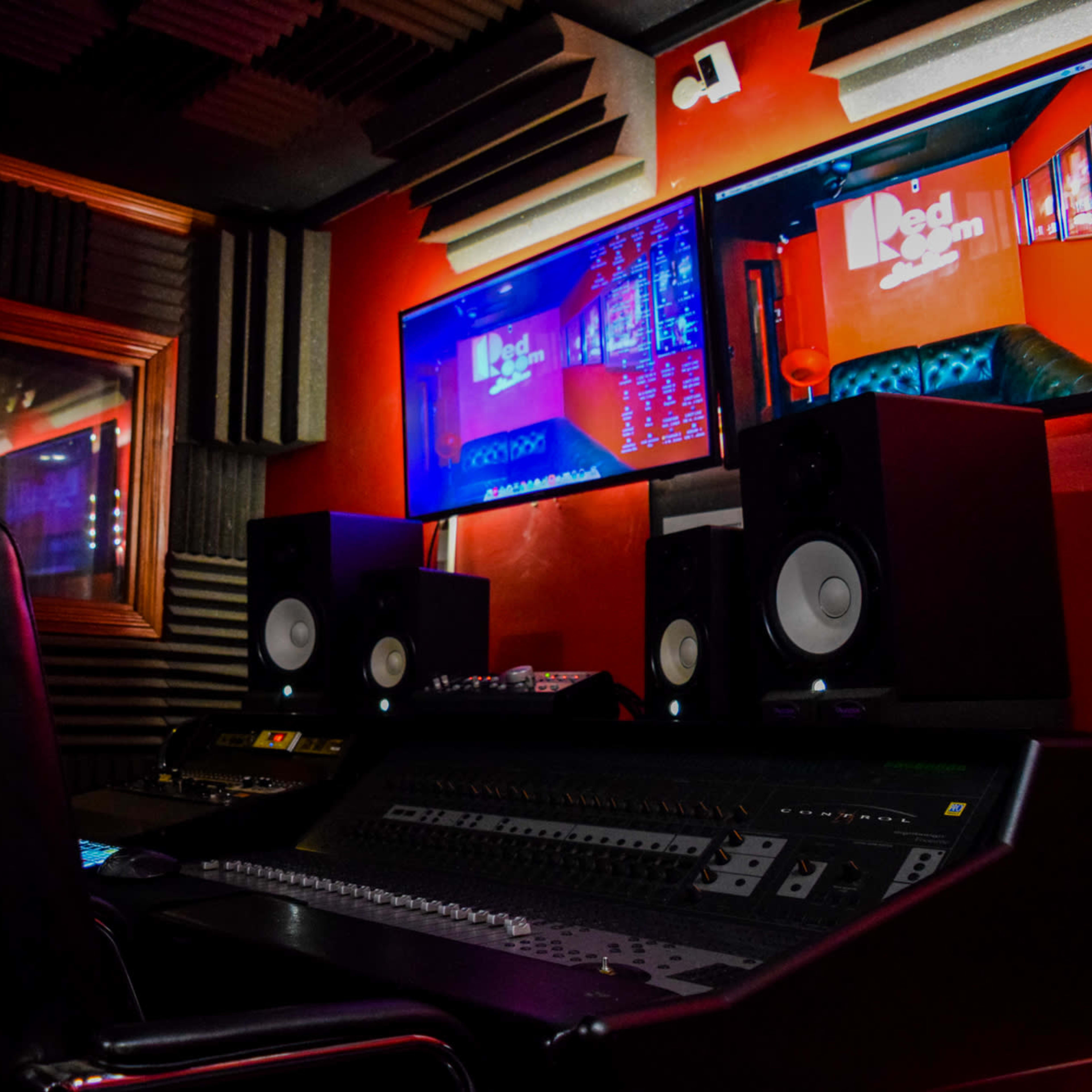 A music recording studio featuring a mixing console, two large speakers, and multiple screens displaying audio tracks.