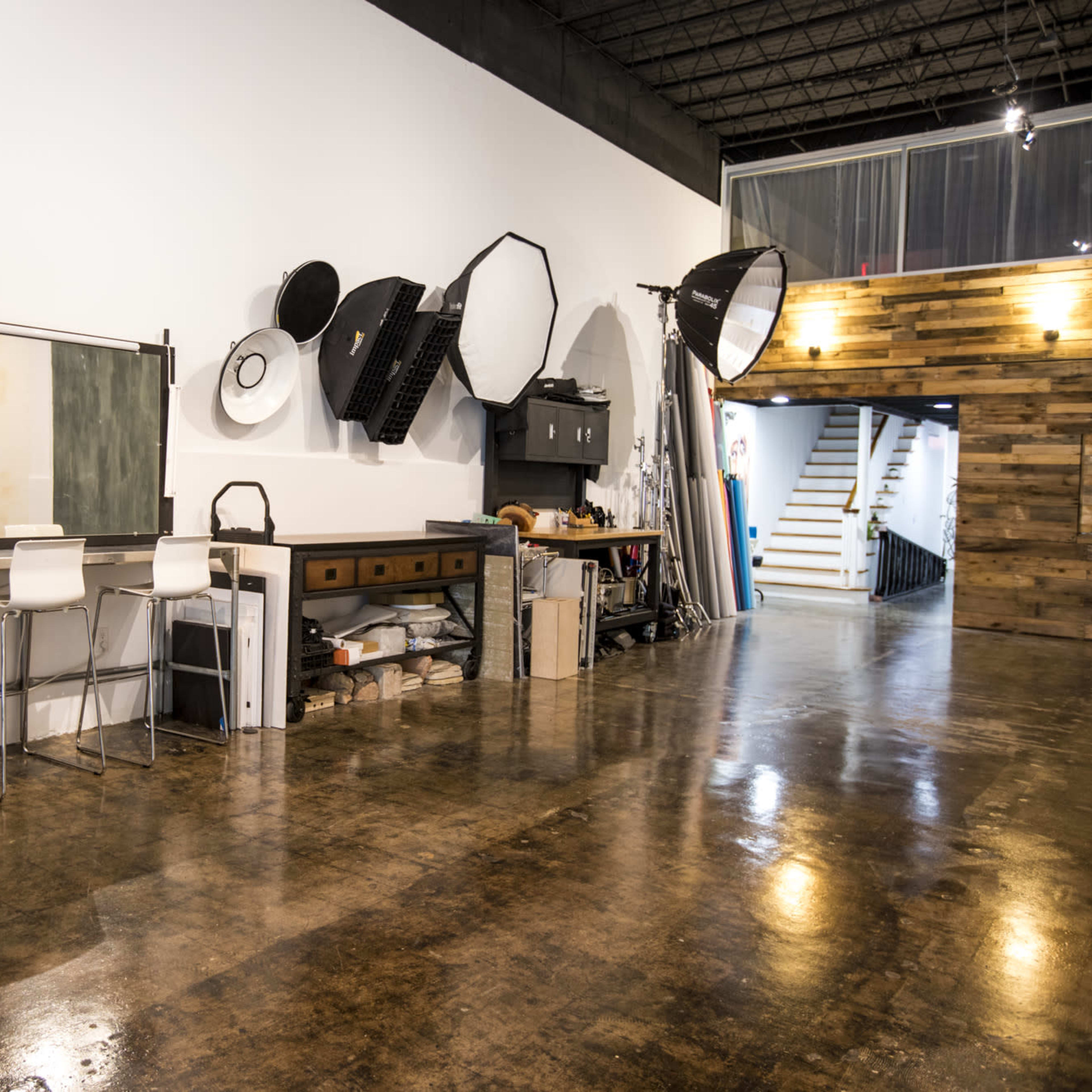 A spacious interior of a studio with a wooden floor, a black and white color scheme, and various photography equipment mounted on the wall.