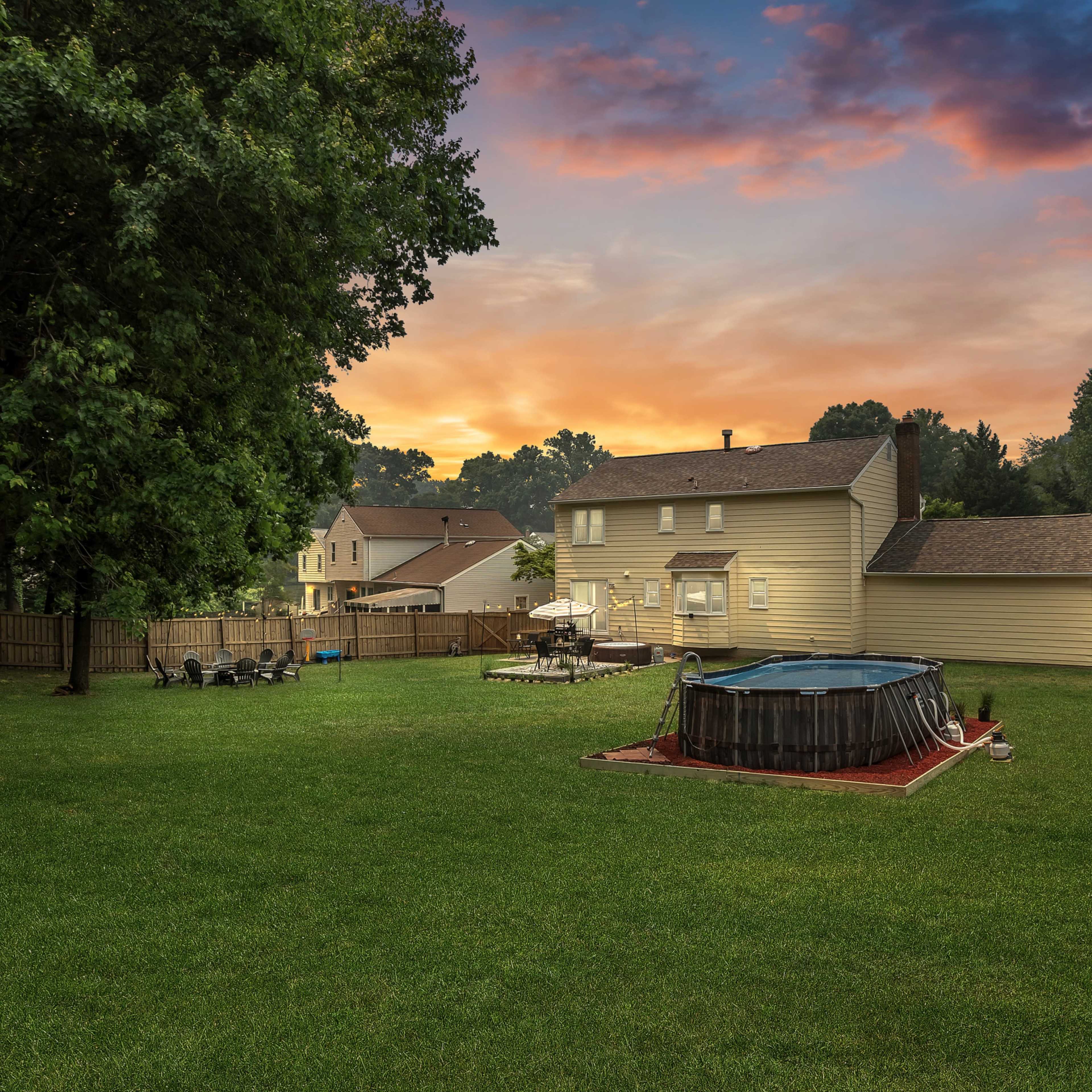 A spacious backyard at sunset, featuring a round above-ground pool and a seating area surrounded by trees and homes in the background.