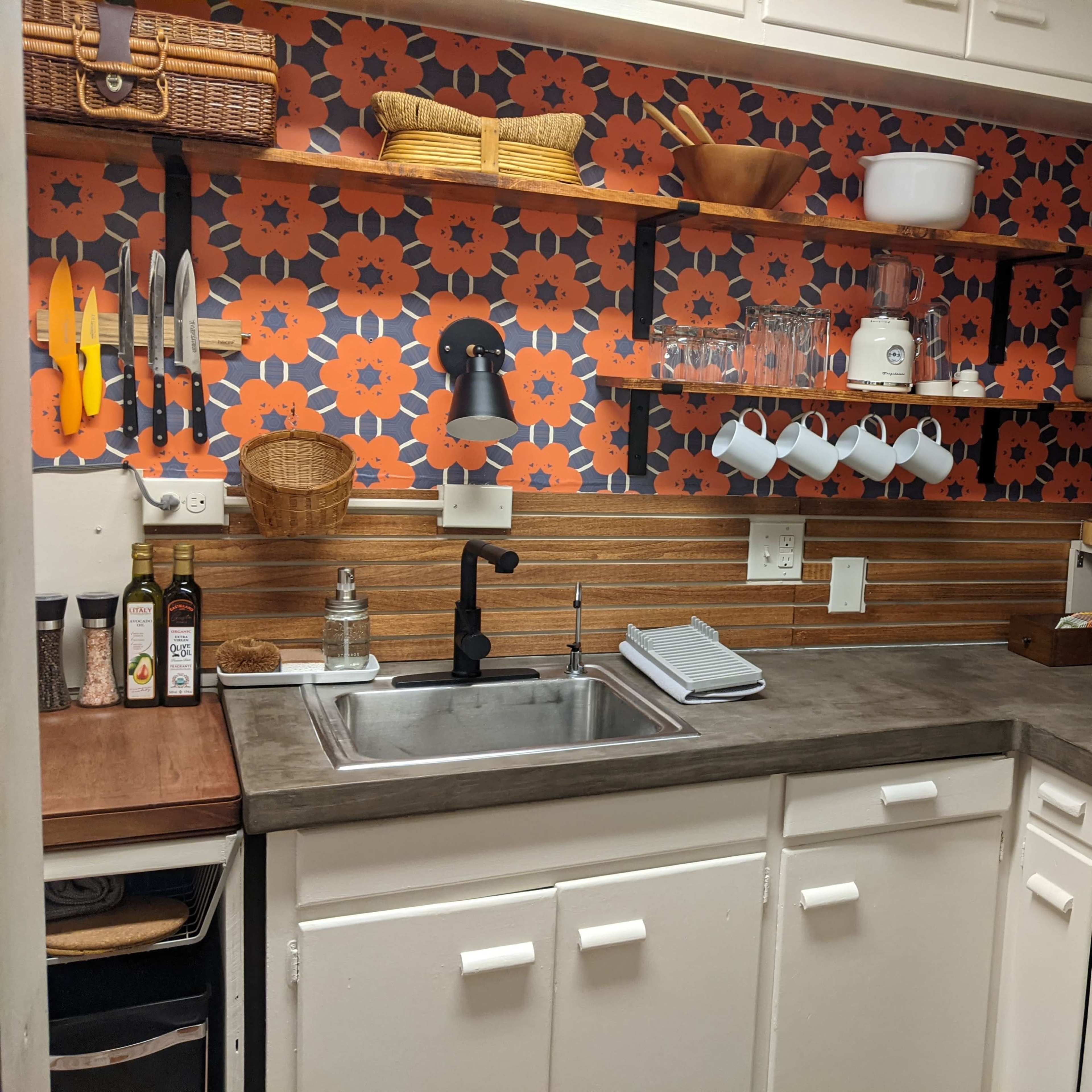 A compact kitchen features a patterned backsplash, open shelving with kitchen items, and a stainless steel sink.