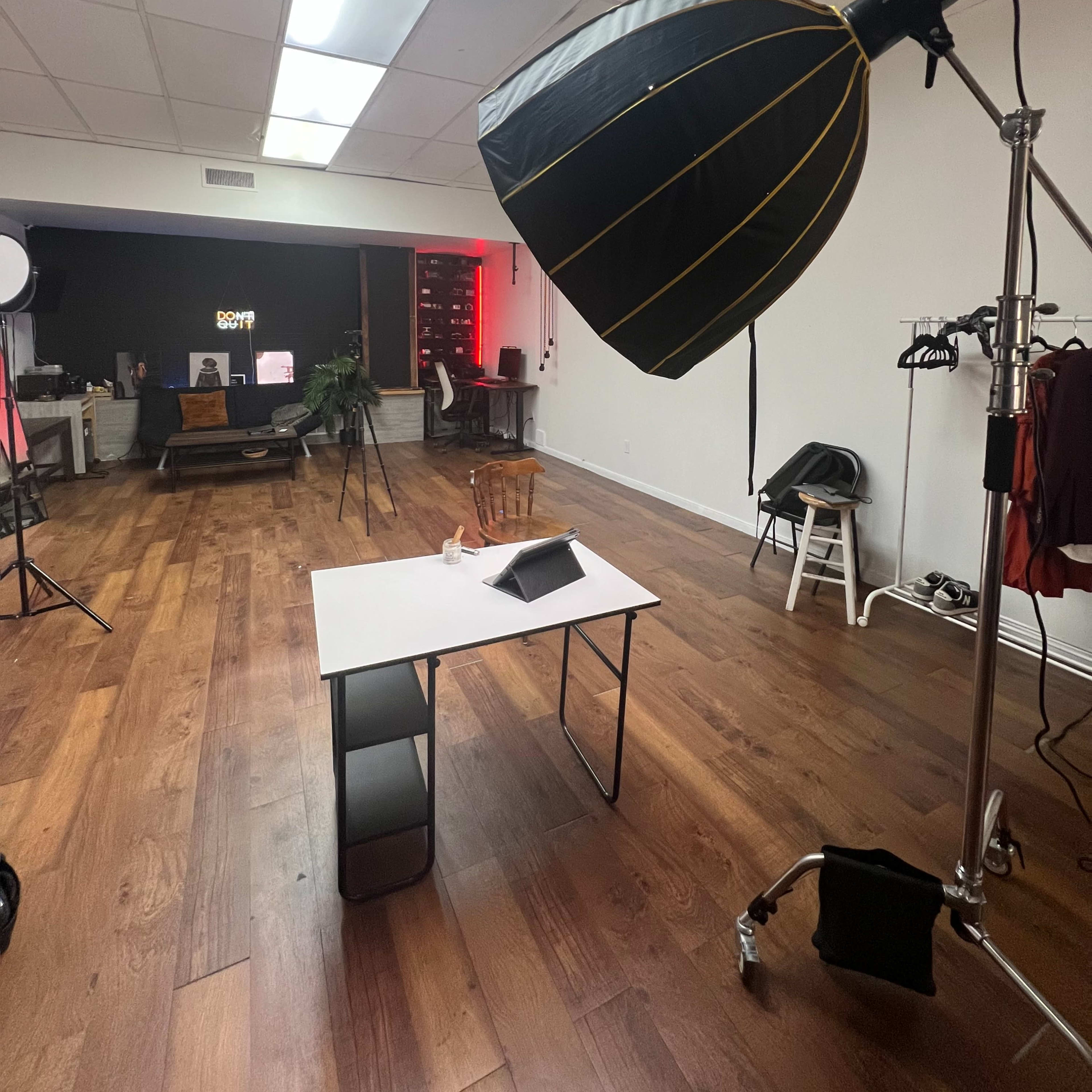 A photo studio is set up with a large softbox light, a table with a tablet on it, and various equipment in the background.