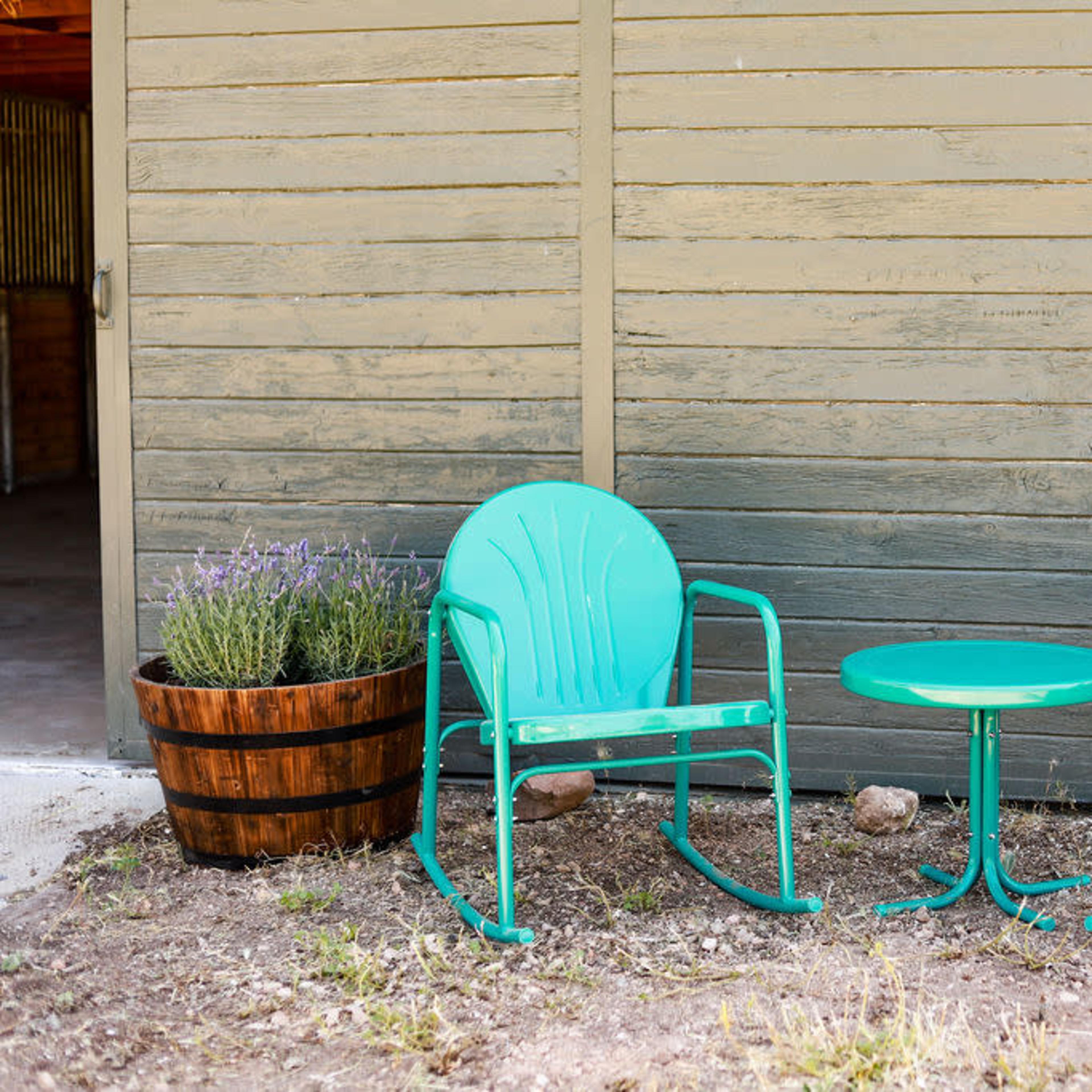 Two turquoise rocking chairs and a matching table sit next to a wooden planter with lavender.