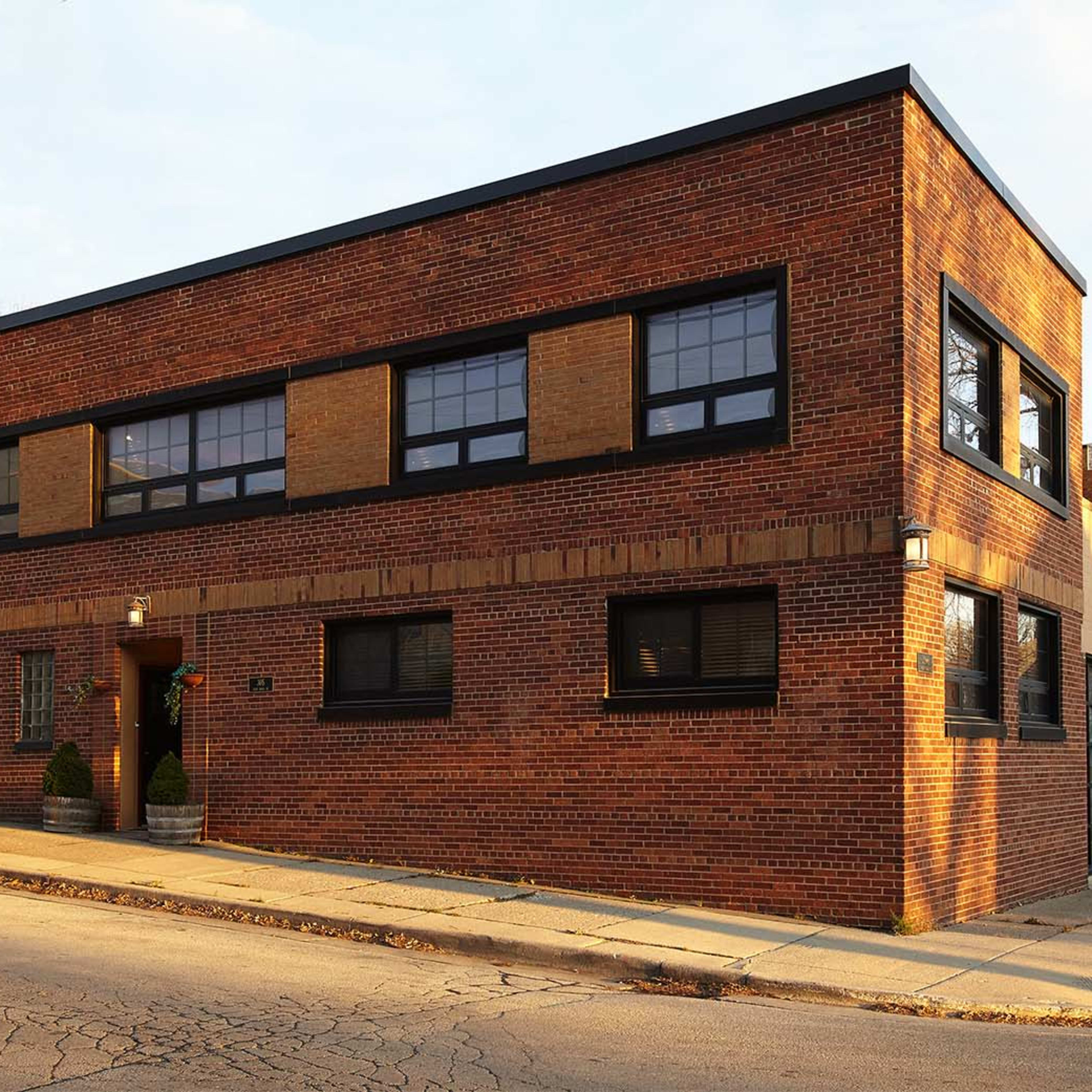 A large, modern brick building with large windows and a flat roof is situated at the corner of a city street.
