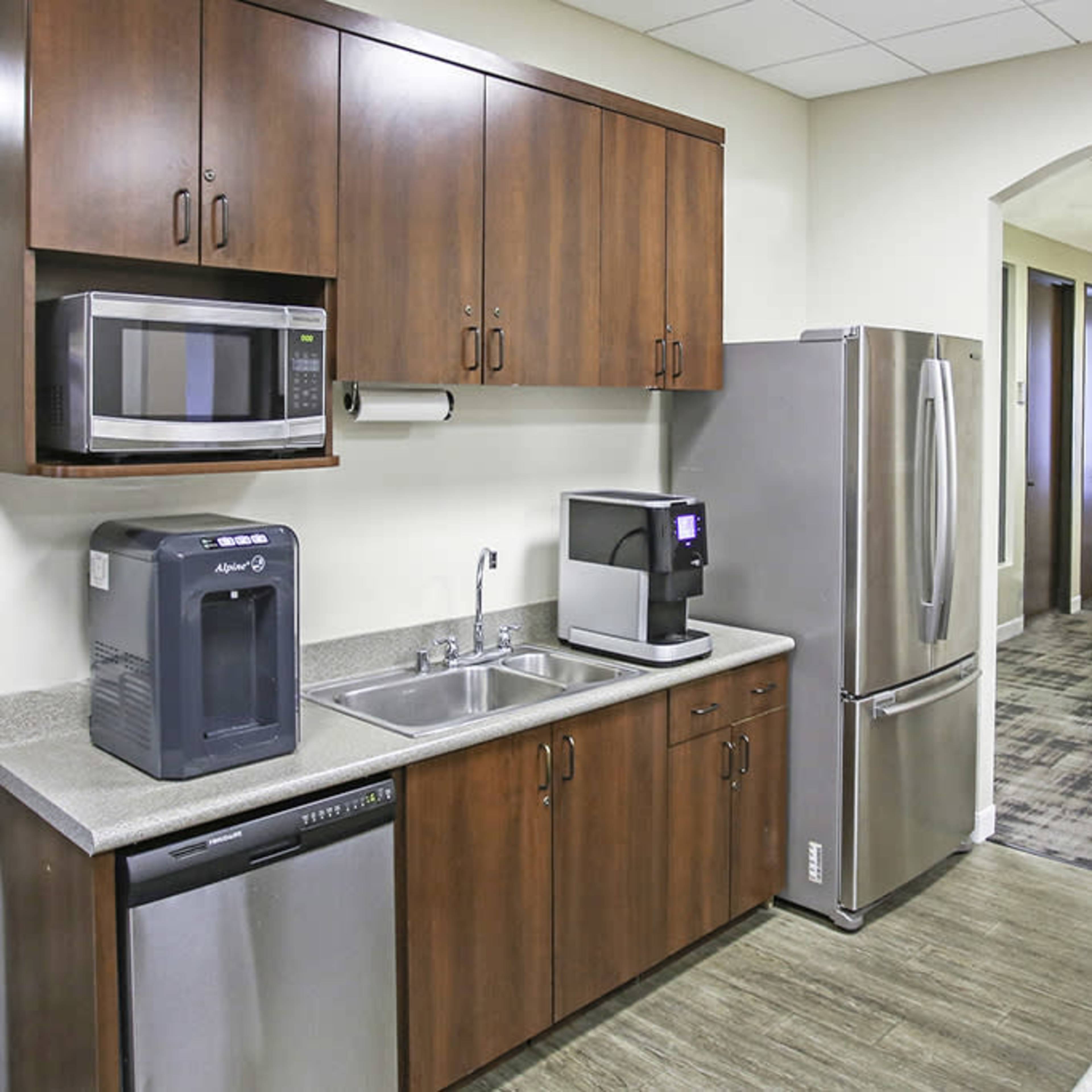 A modern kitchenette with wooden cabinets, stainless steel appliances, and a countertop displaying baked goods.