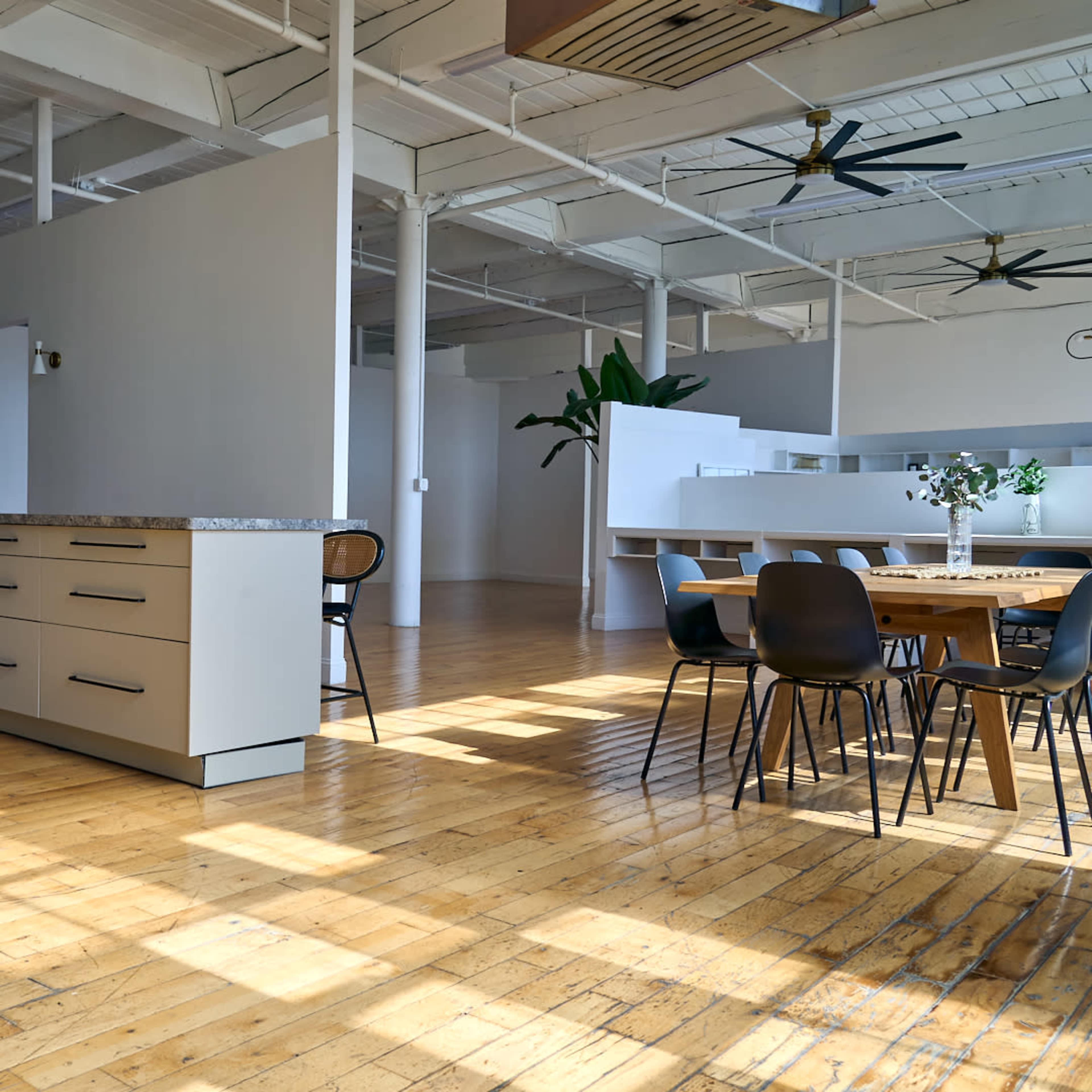 A spacious kitchen and dining area with a large wooden table and modern appliances in an open-concept loft featuring ample natural light.