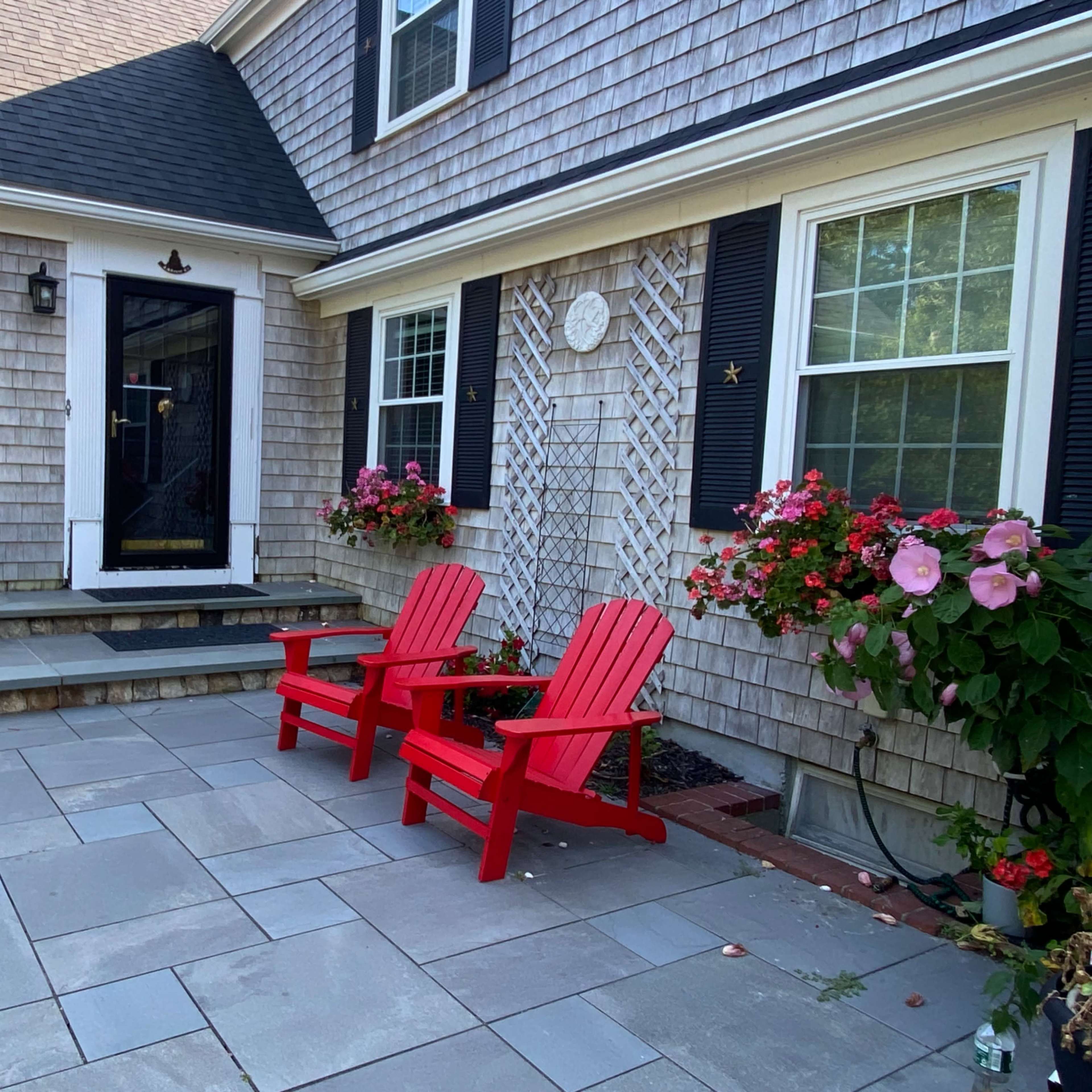 The patio features two red Adirondack chairs and a seating area surrounded by flowering planters and a stone walkway.