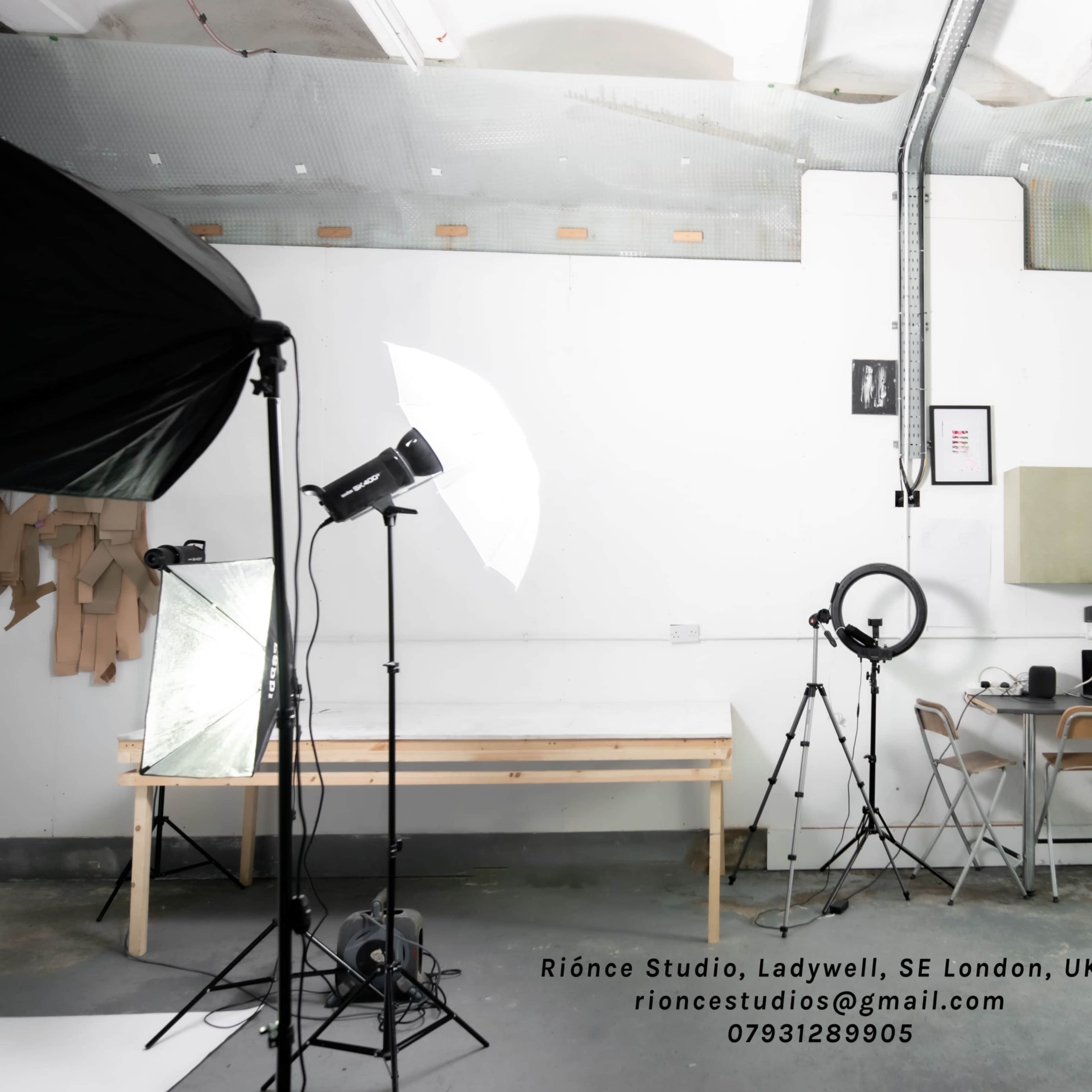 A well-lit studio space in London with a minimalist design, featuring a kitchen area, a photography light setup, and a worktable.