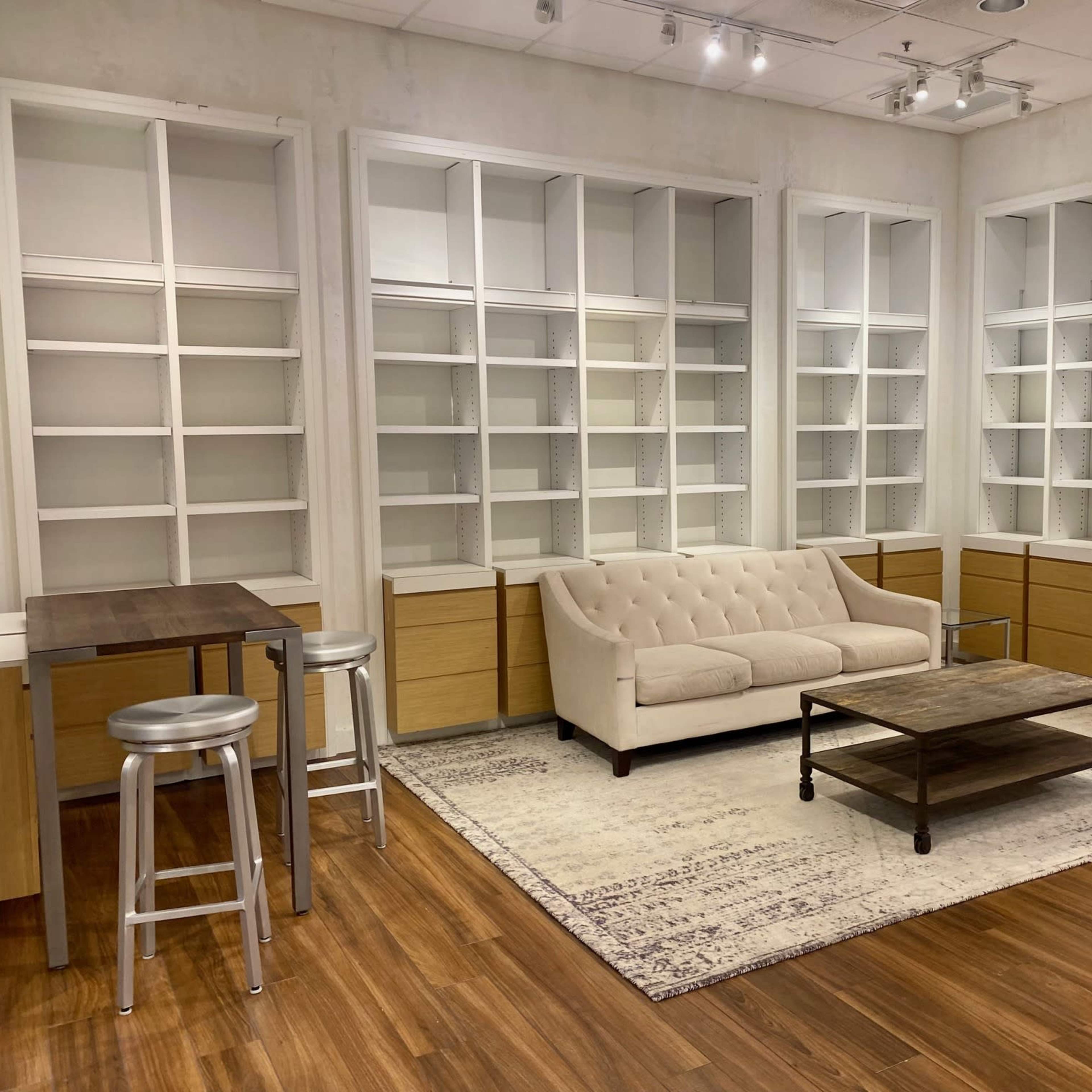 A modern room with a beige couch, a coffee table, and built-in shelving units, along with tall stools and small tables on a wooden floor.