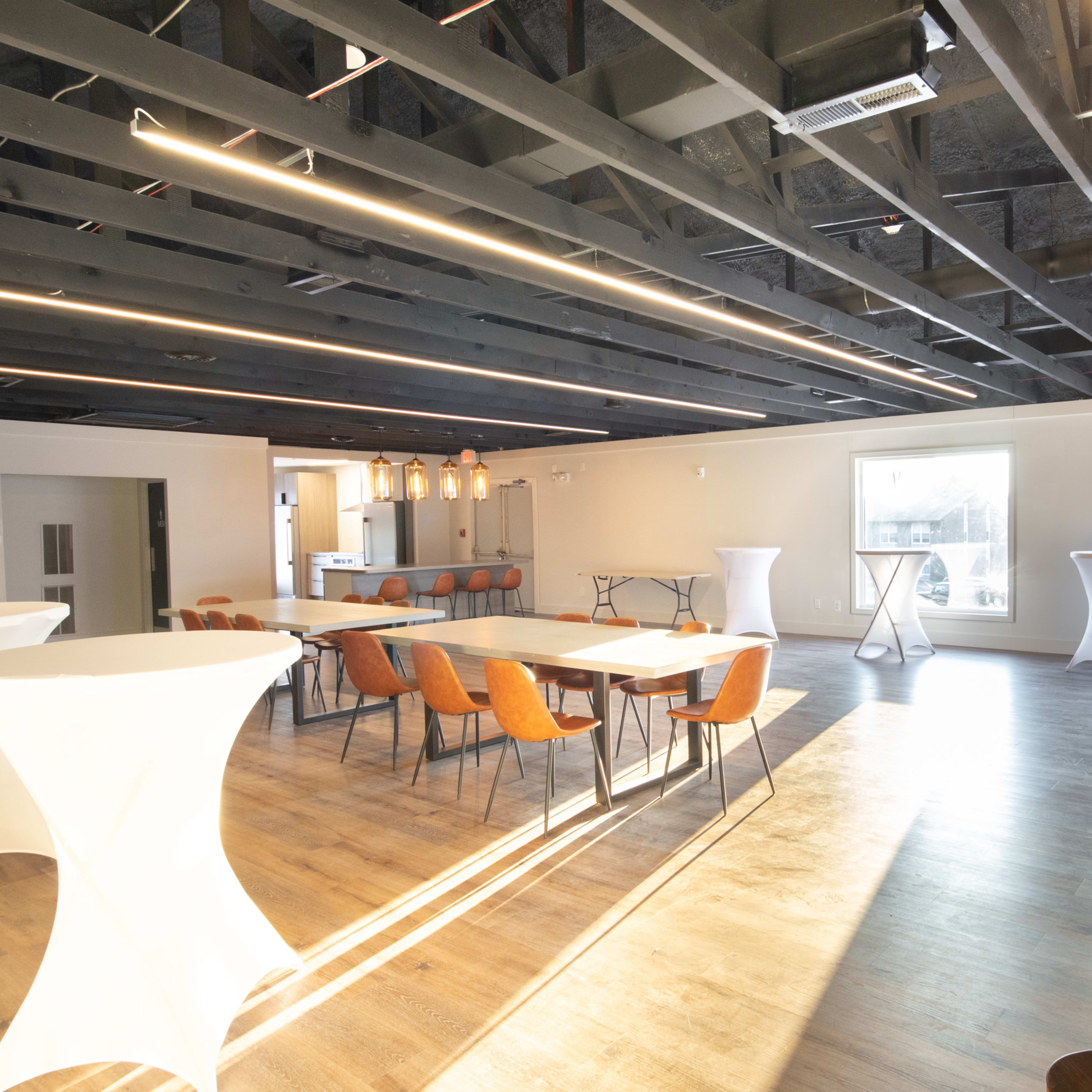A spacious event venue with modern lighting, wooden floors, and various seating arrangements, including tables and high-top cocktail tables.