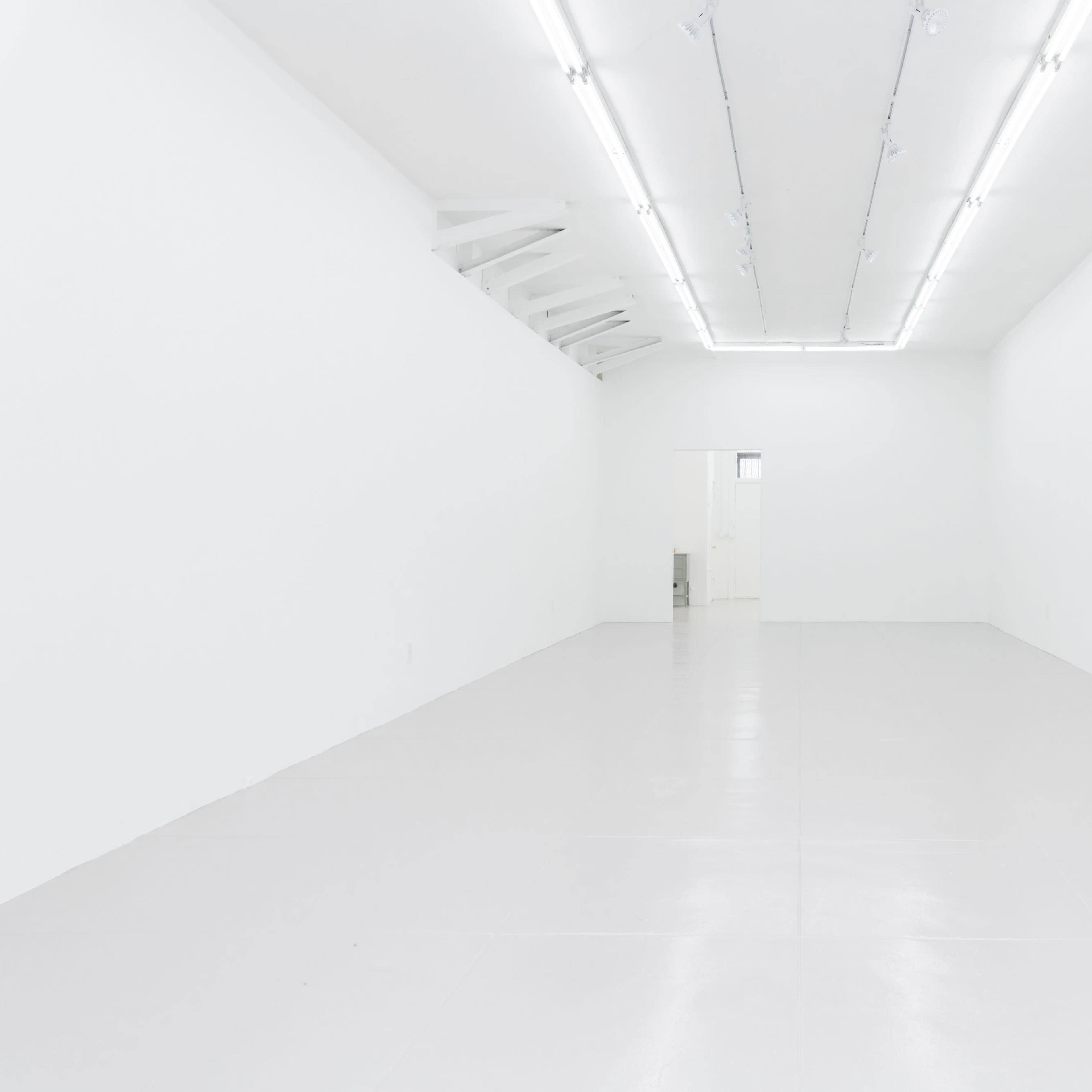 A stark, empty white room with a polished floor and bright fluorescent ceiling lights.