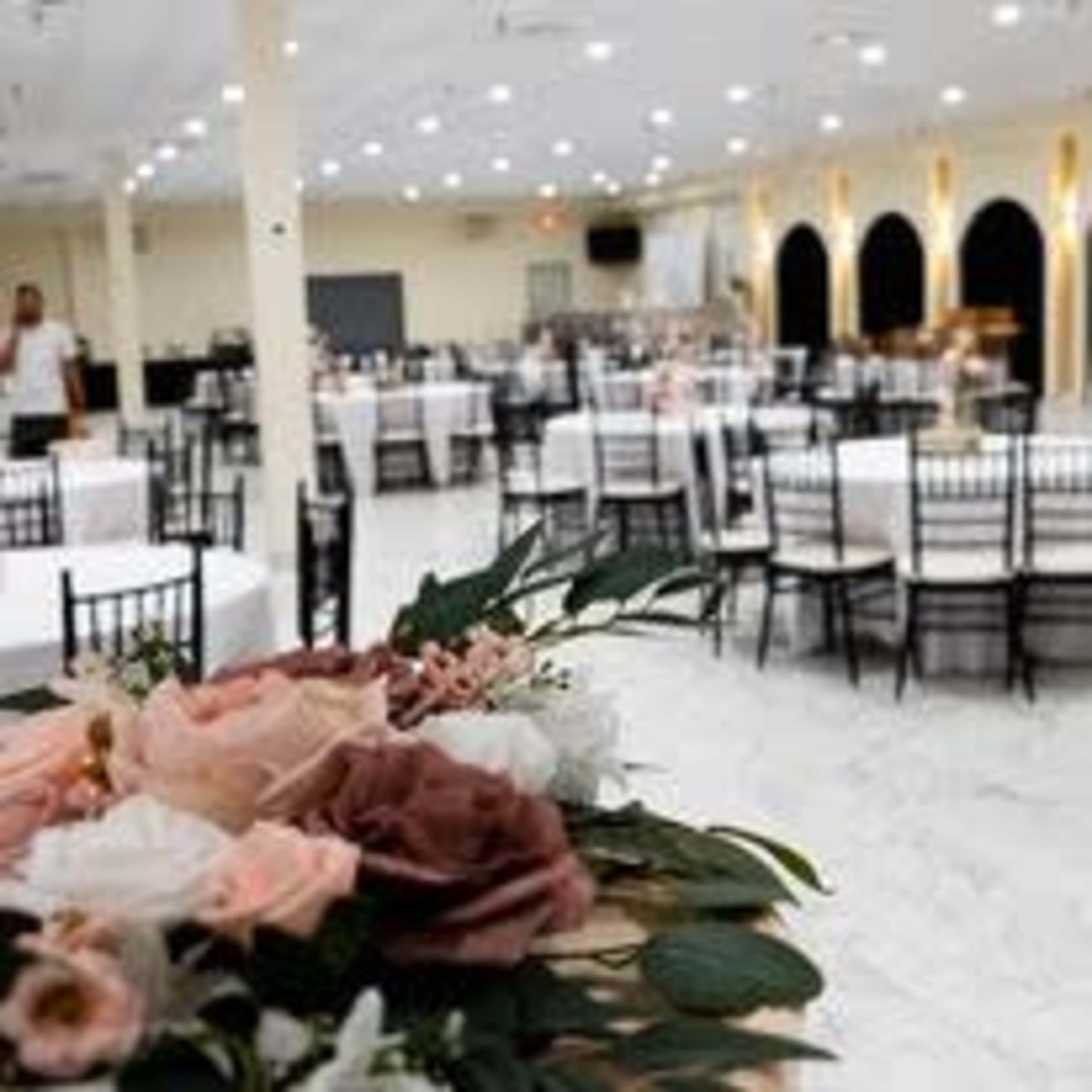A spacious banquet hall with neatly arranged tables and chairs, decorated with floral centerpieces.