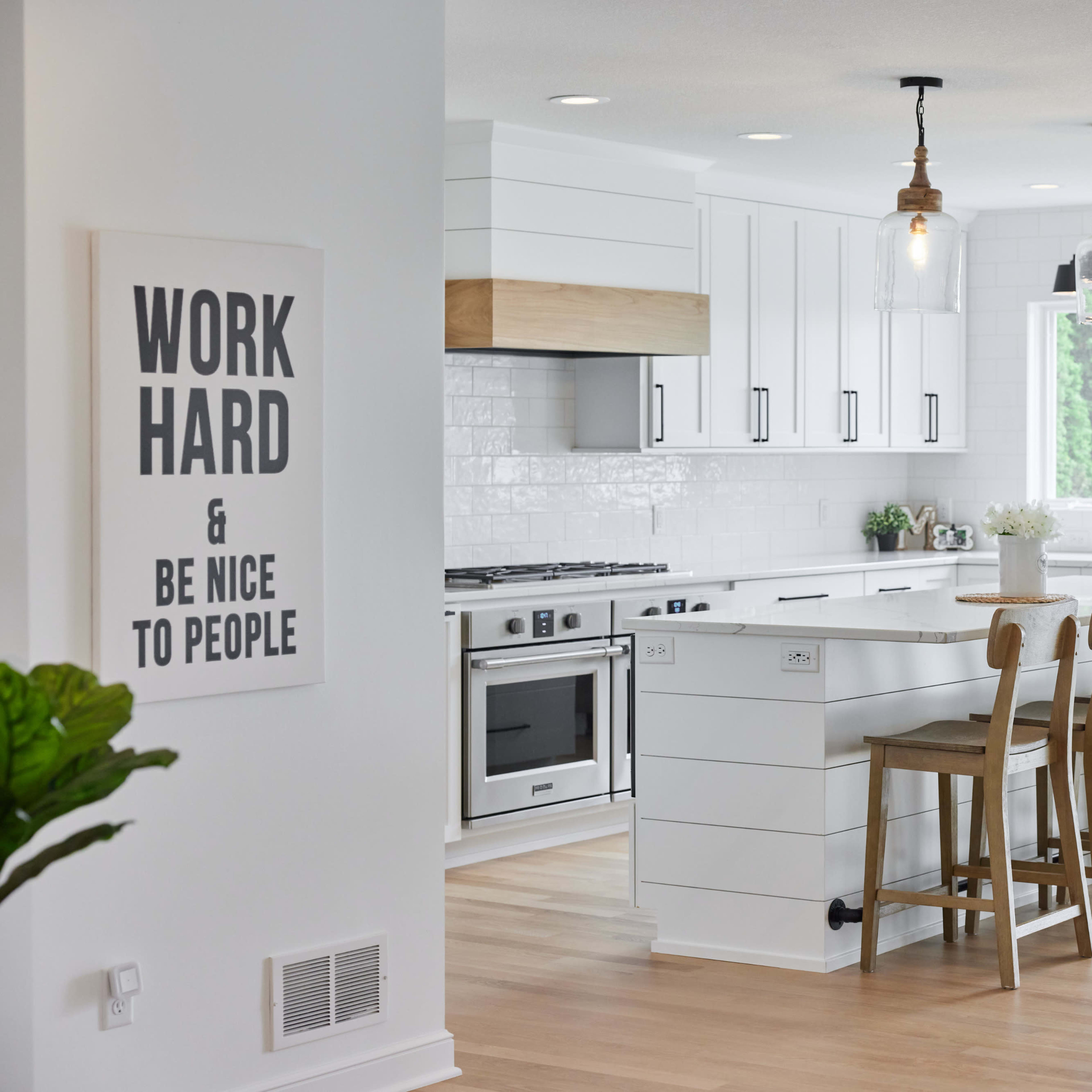 A modern kitchen featuring white cabinetry, a large island with wooden stools, and large windows letting in natural light.