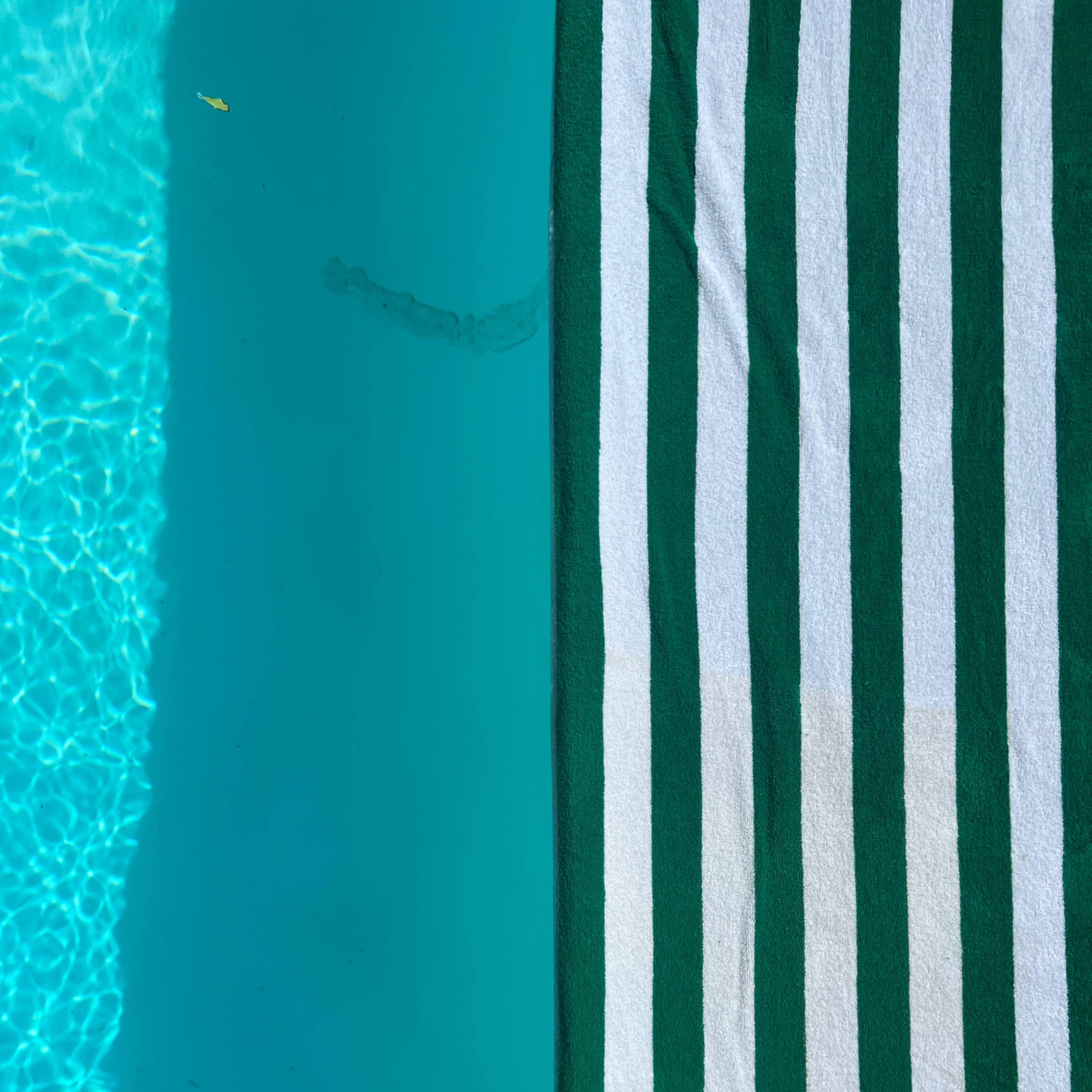 A green and white striped towel is positioned along the edge of a swimming pool with clear blue water.