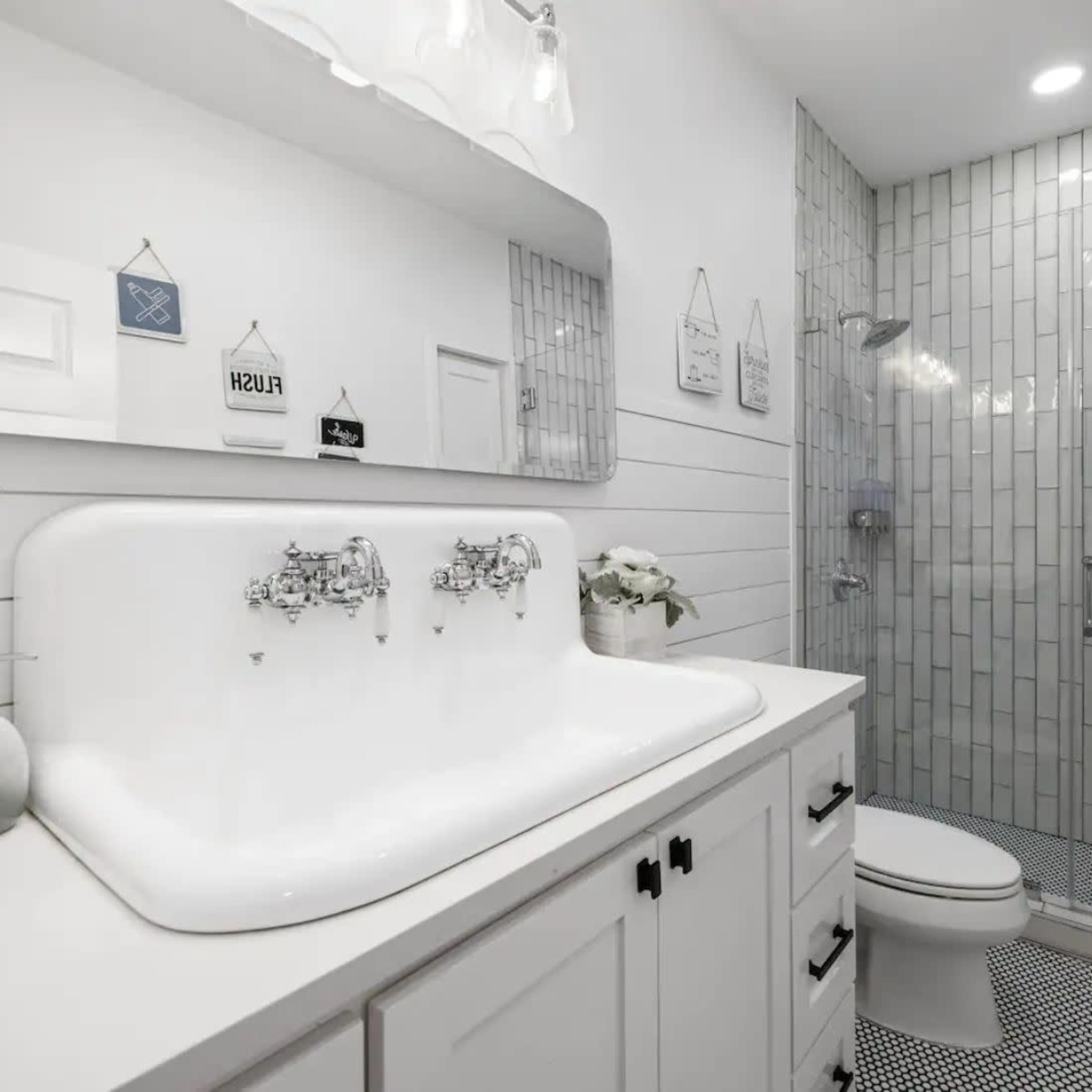A modern bathroom featuring a white vanity with a double sink, a large mirror, and a glass-enclosed shower with gray tile walls.