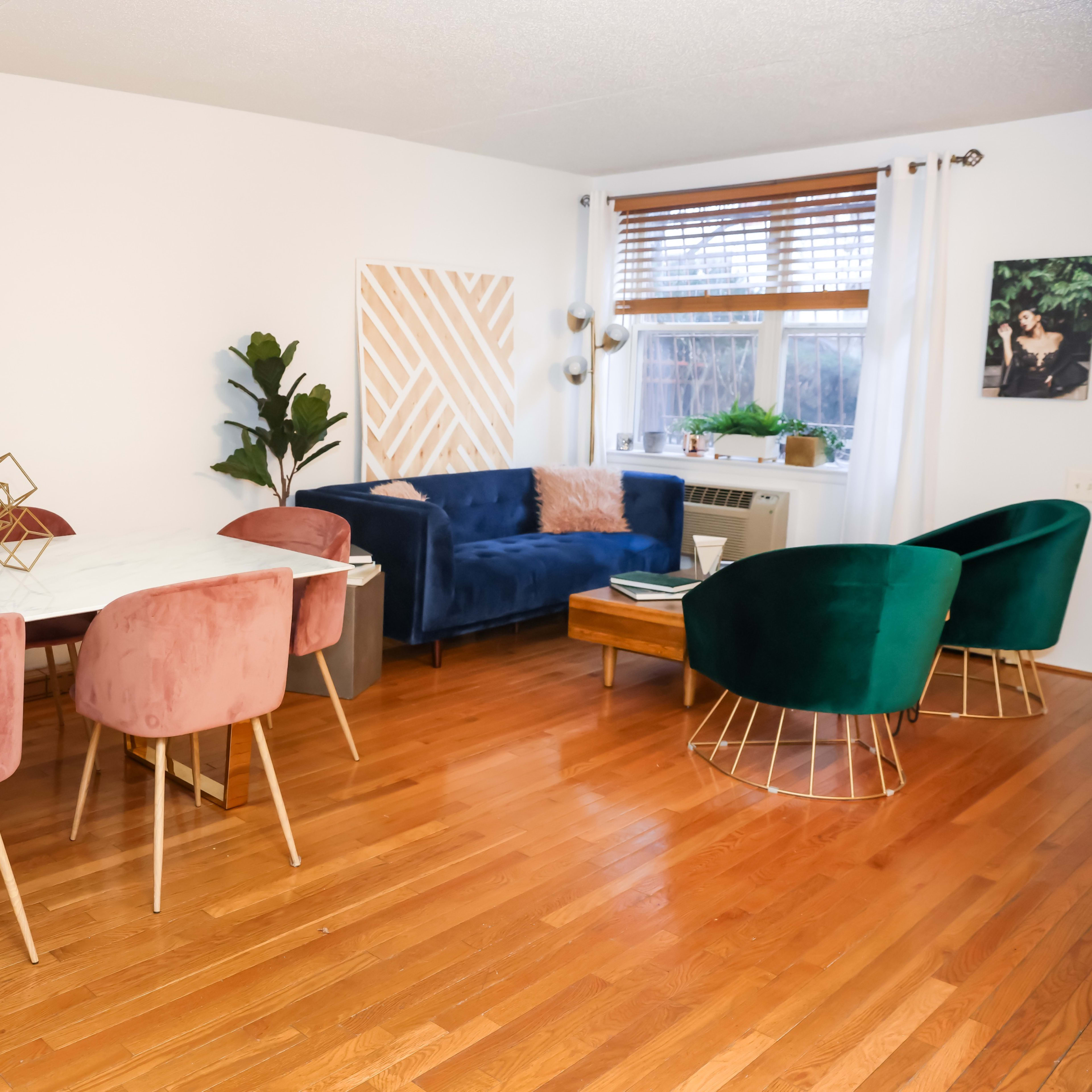 A dining area with a marble table and pink upholstered chairs, adjacent to a living space featuring a blue sofa and green accent chairs.