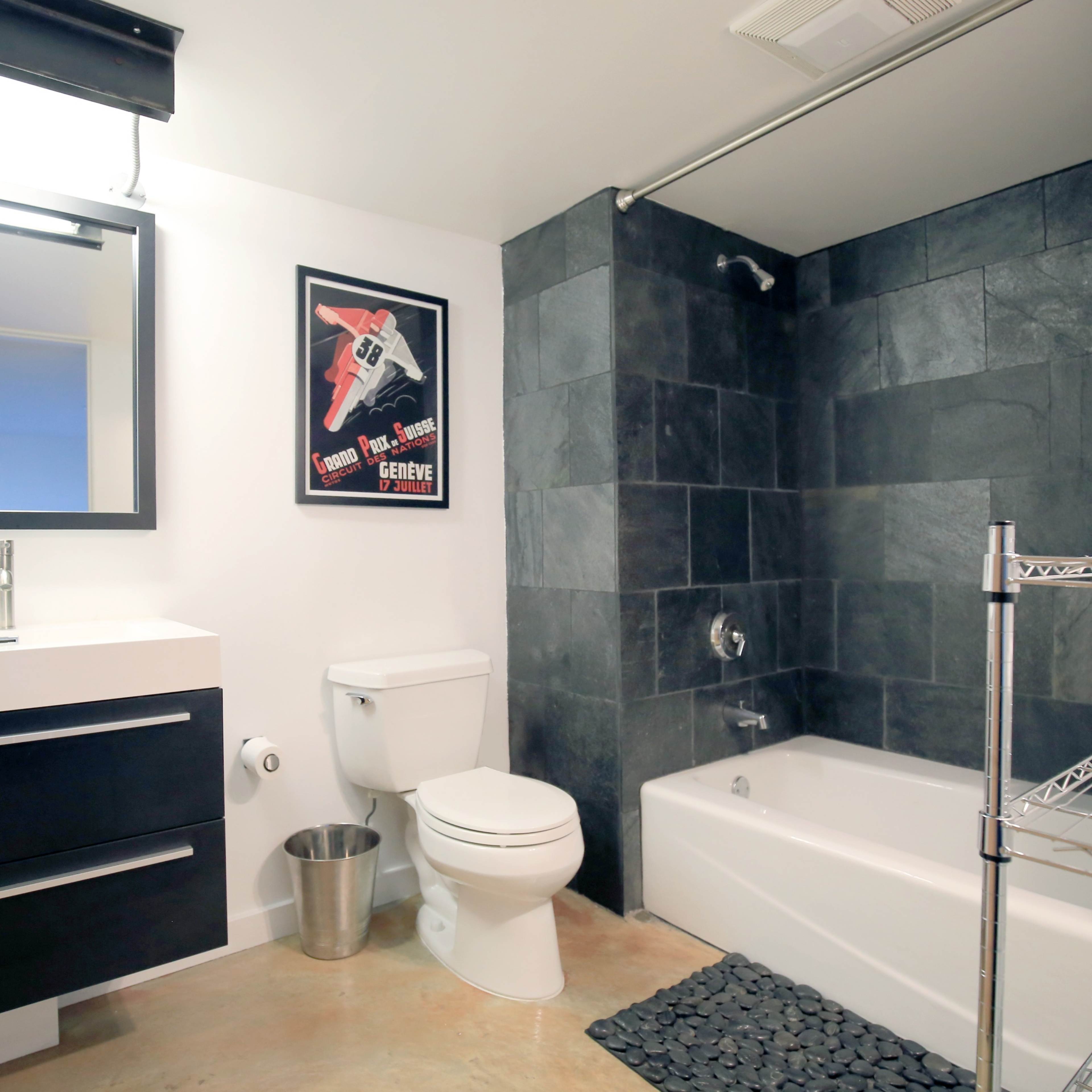 A modern bathroom featuring a bathtub, a wall-mounted sink with a cabinet, a toilet, and slate tile accents.