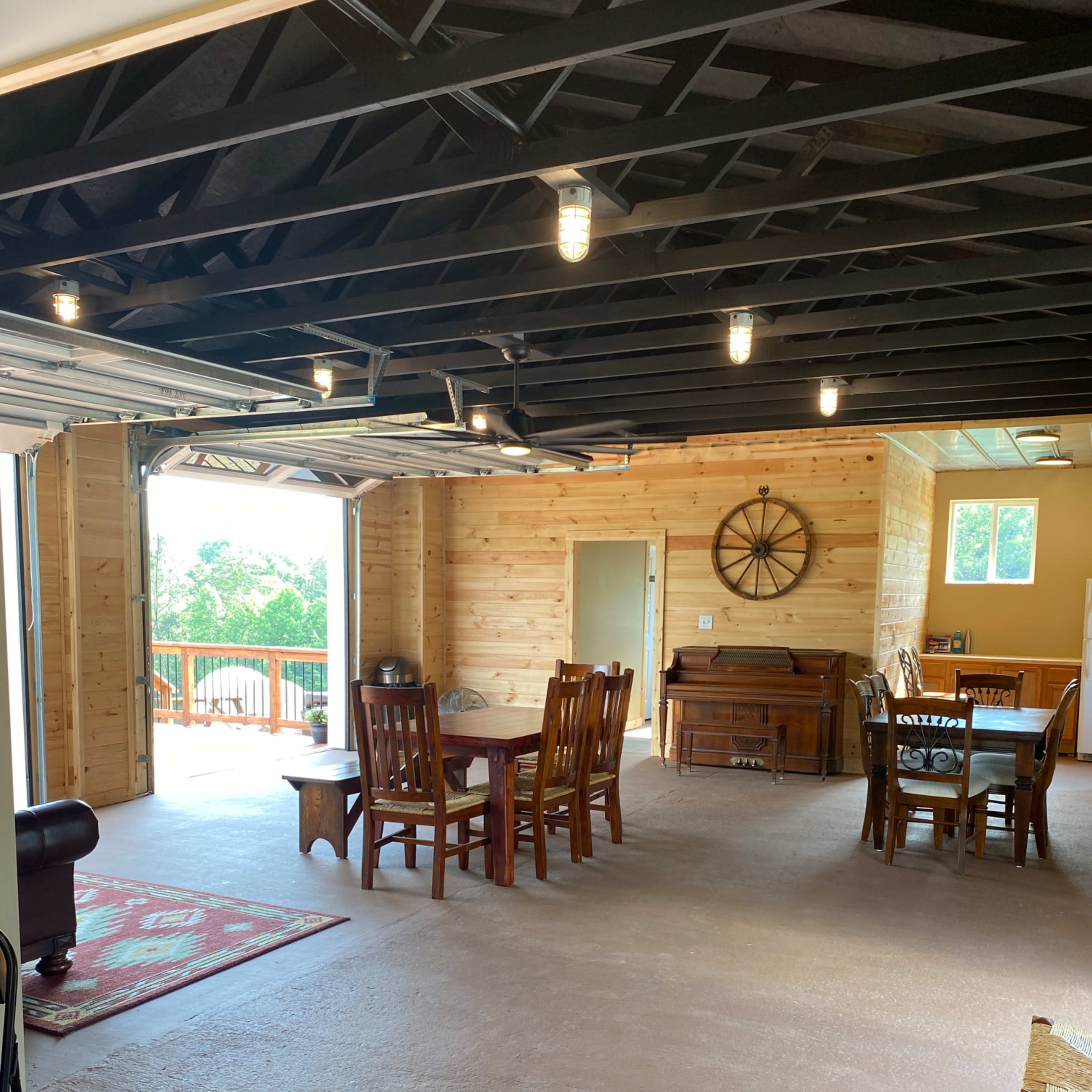 A spacious interior room featuring wooden dining furniture, a piano, and large windows that open to a view outside.