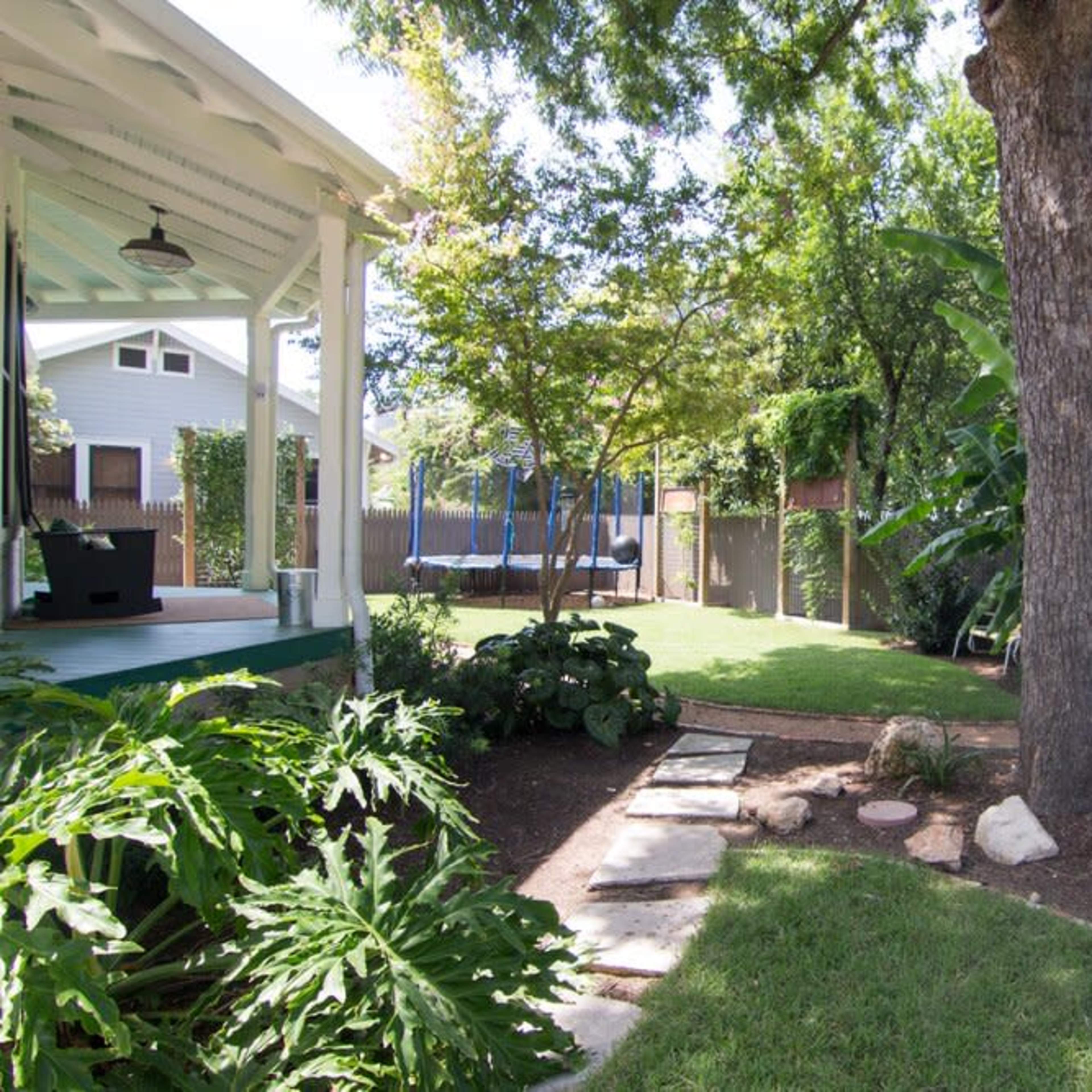 A backyard garden with a stone pathway leading to a grassy area, surrounded by trees and plants.