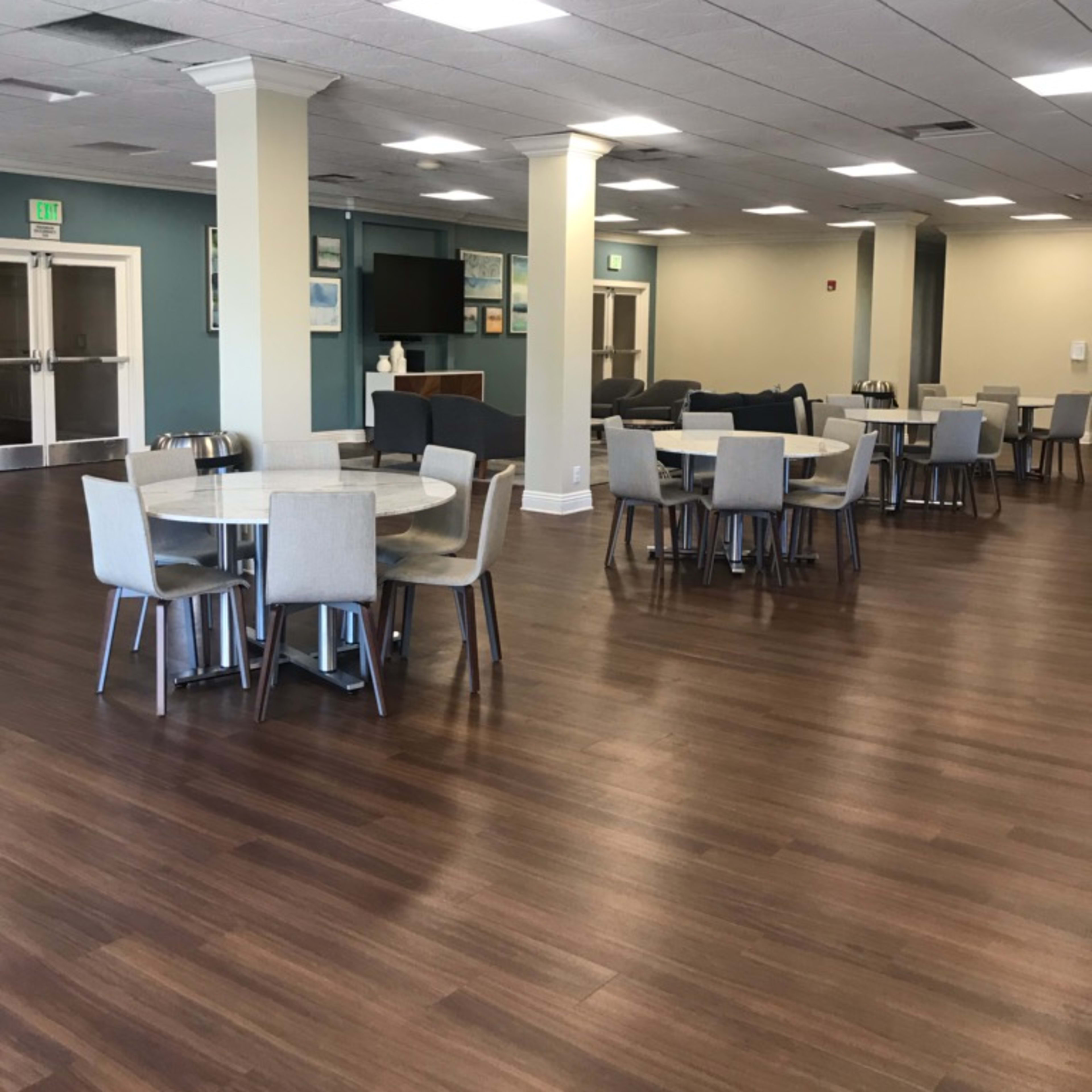 A spacious, well-lit dining area featuring several round tables with chairs and a service counter in the background.