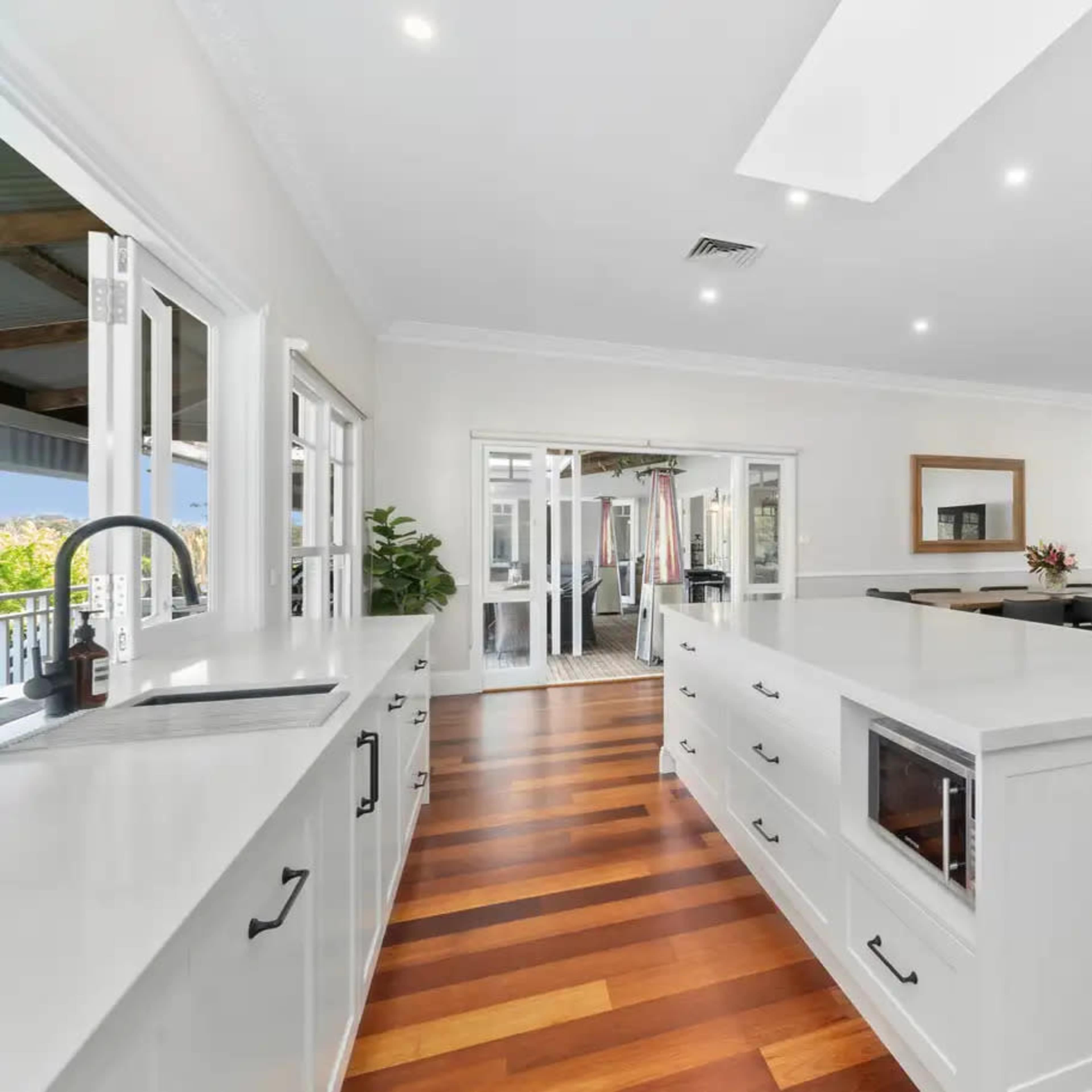 A modern, spacious kitchen with an island, featuring white cabinetry and wooden flooring.