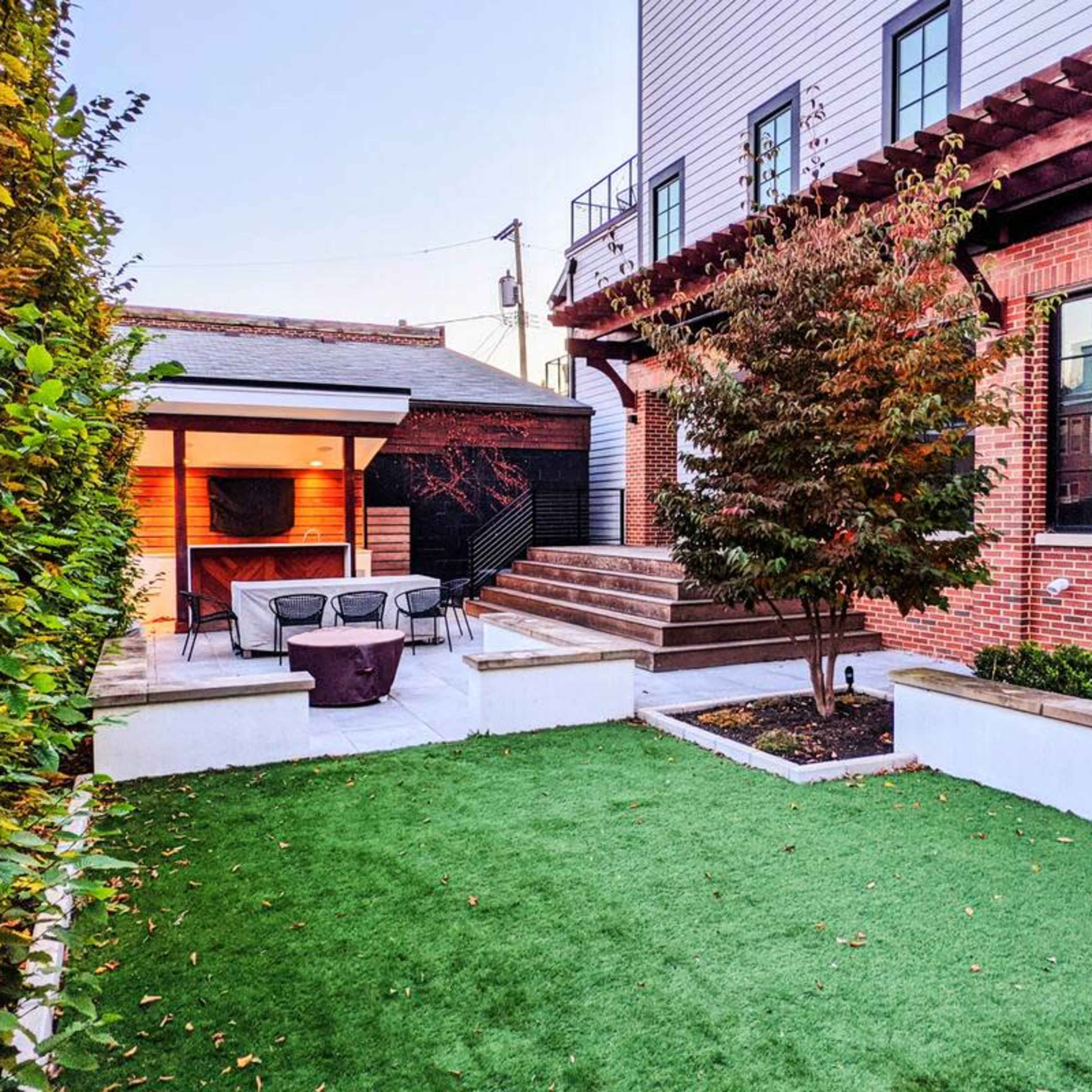 A well-maintained backyard featuring green grass, a patio with outdoor seating, and a landscaped area with trees and shrubs.