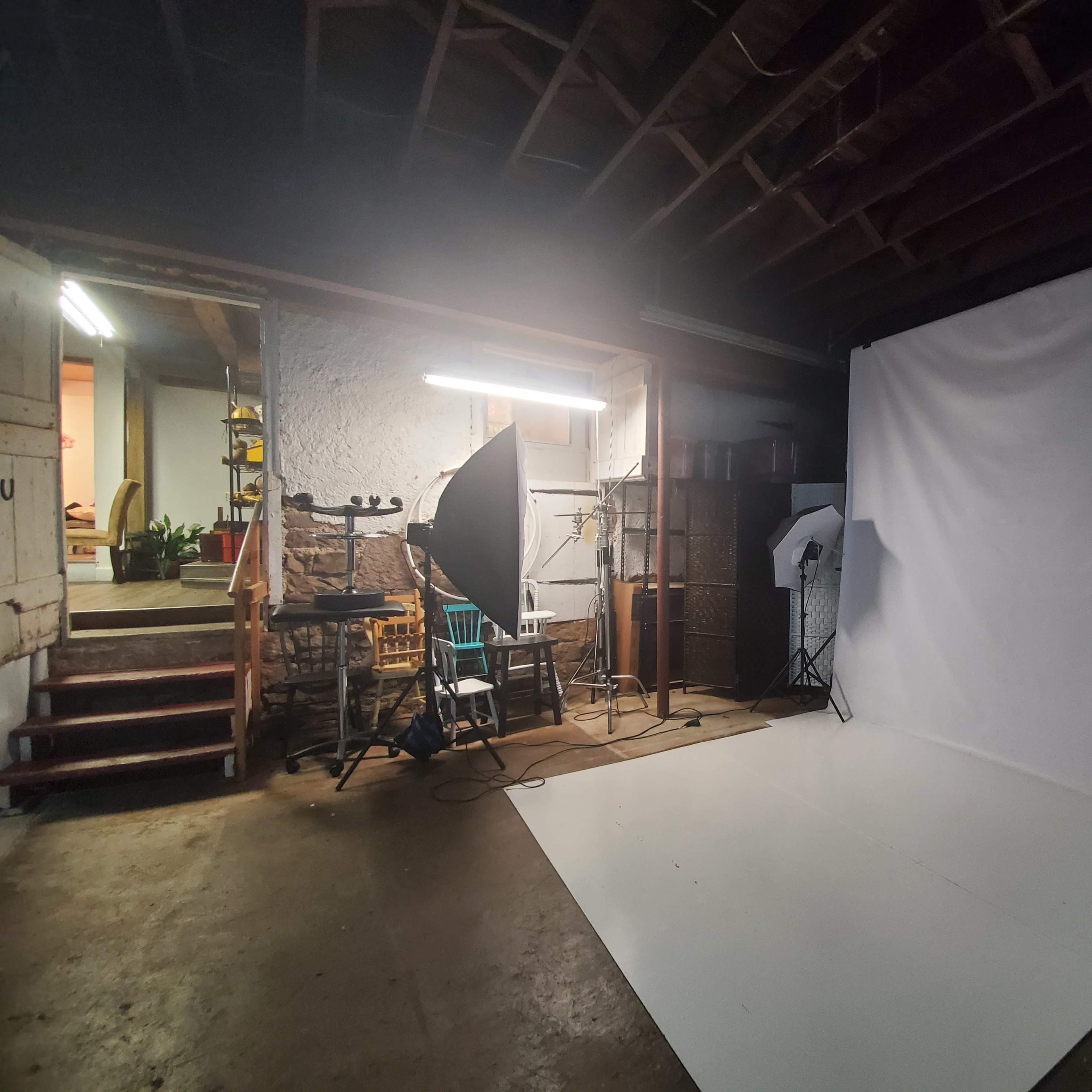 A photo studio setup featuring a white backdrop, lighting equipment, and a staircase leading to a different area.