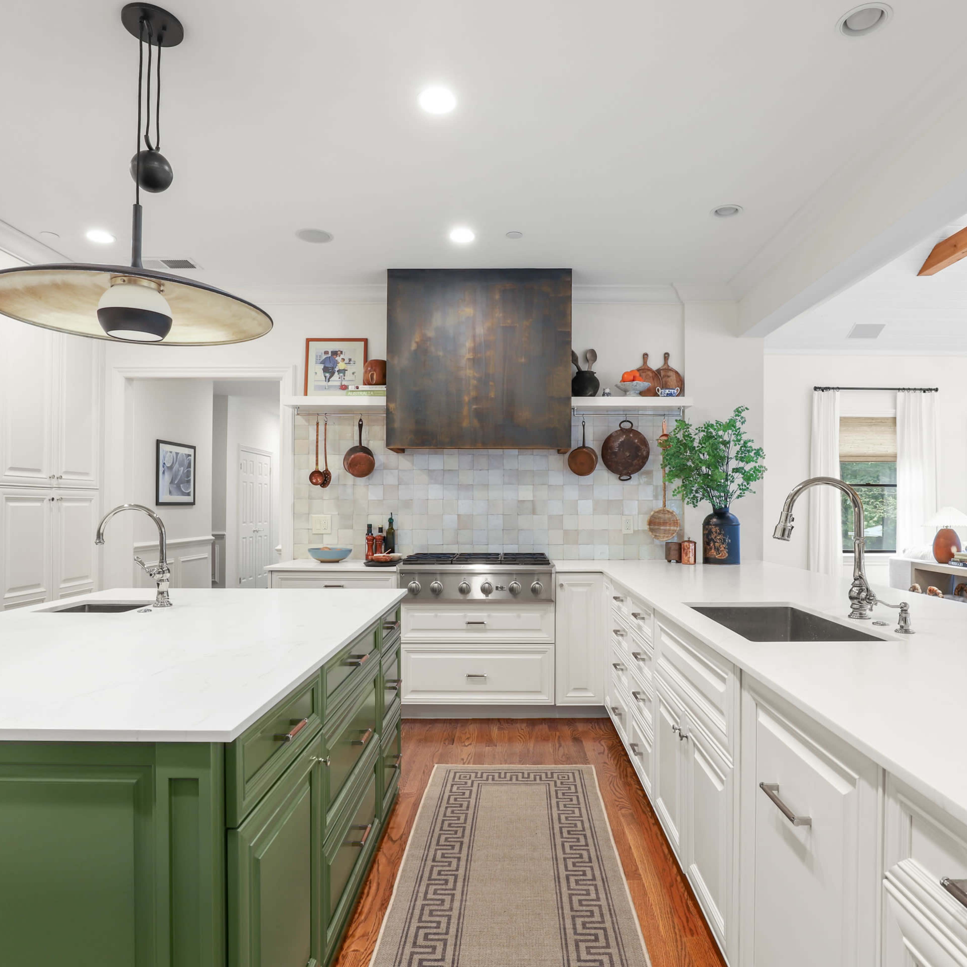 A modern kitchen features white cabinetry, a central green island, and a stainless steel range hood above the stove.