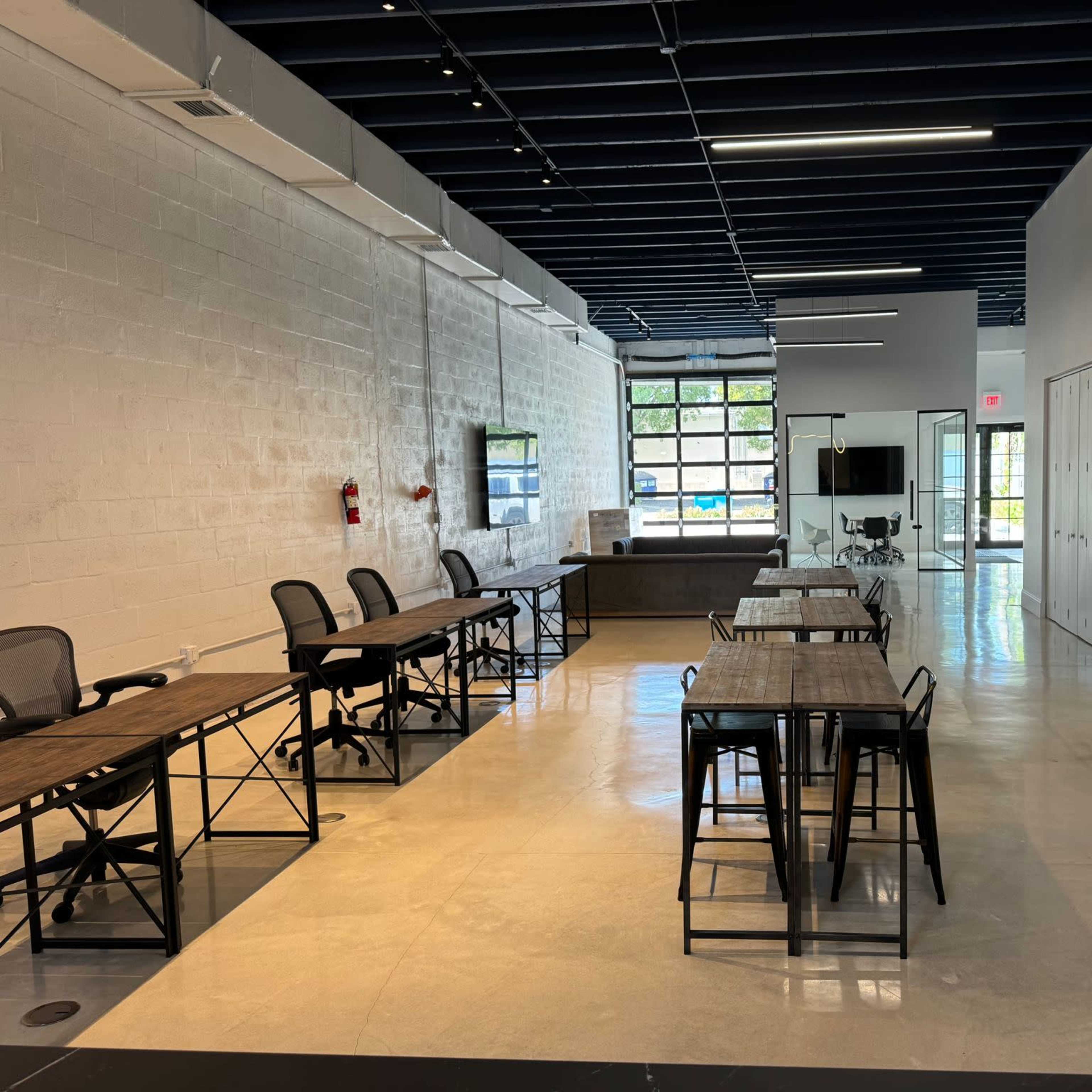 A spacious office interior with several tables and chairs arranged in a well-lit environment featuring large windows and a modern design.