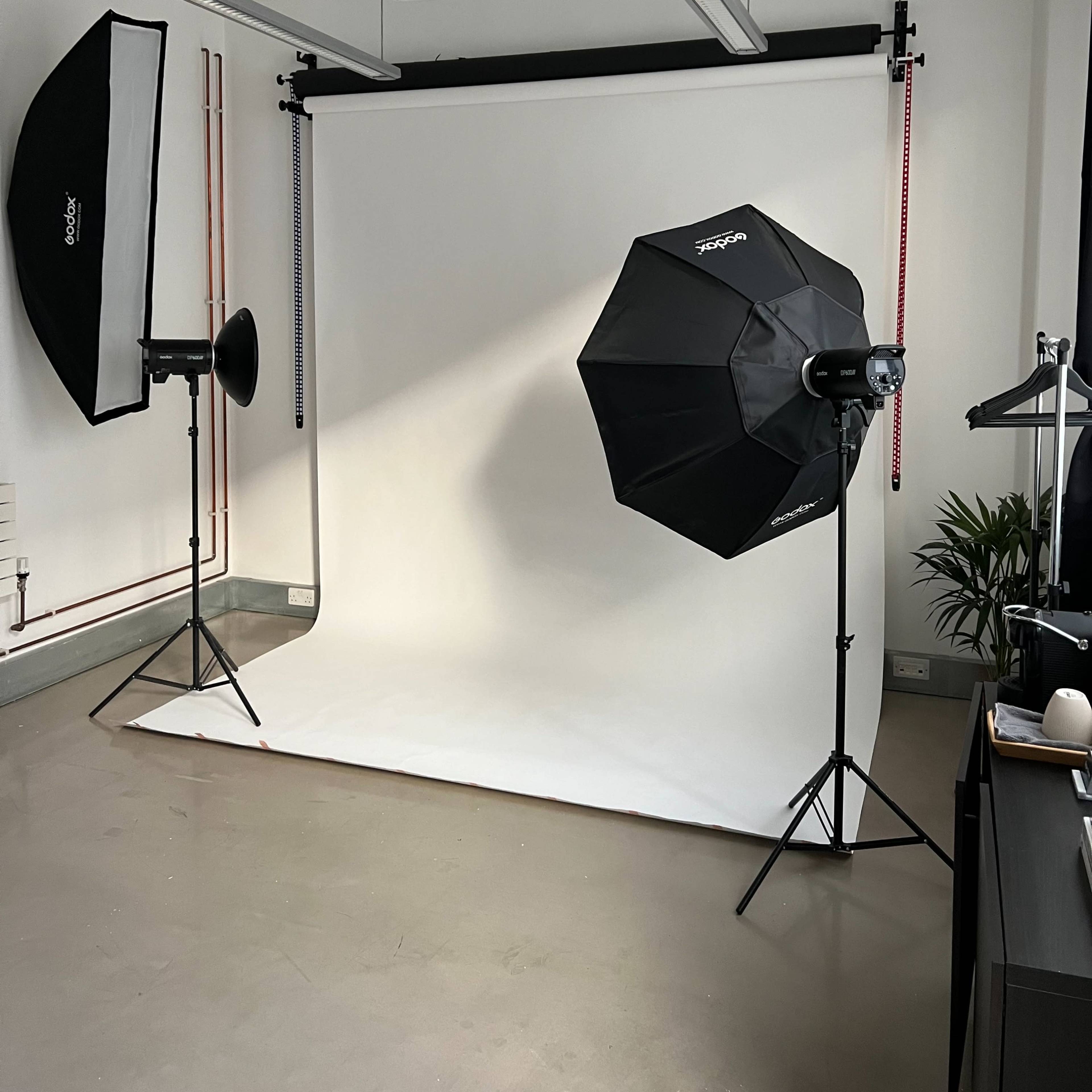 A photography studio with two lighting setups and a white backdrop against a plain floor.