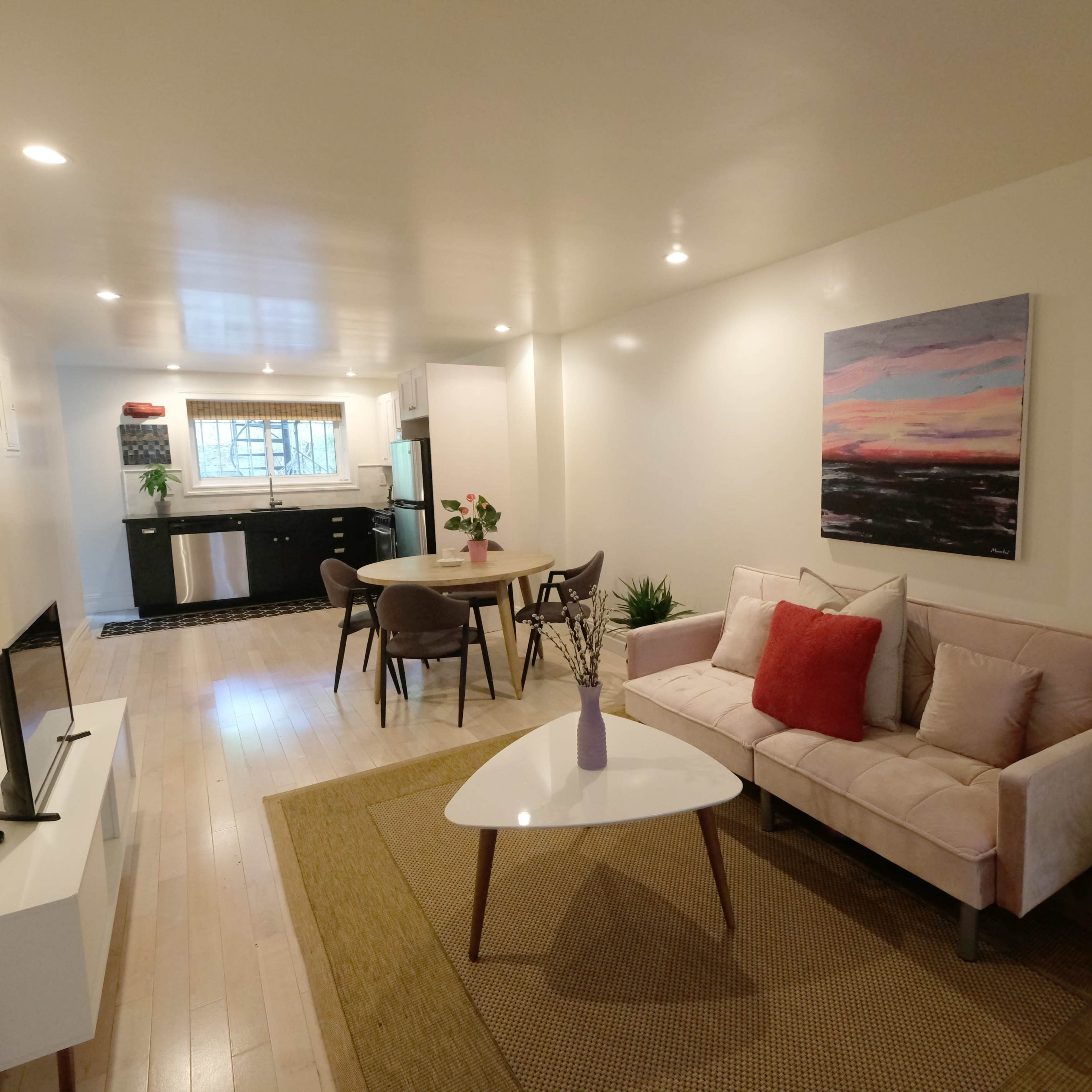 A modern living space features a light-colored sofa, a round dining table, and a kitchen visible in the background.
