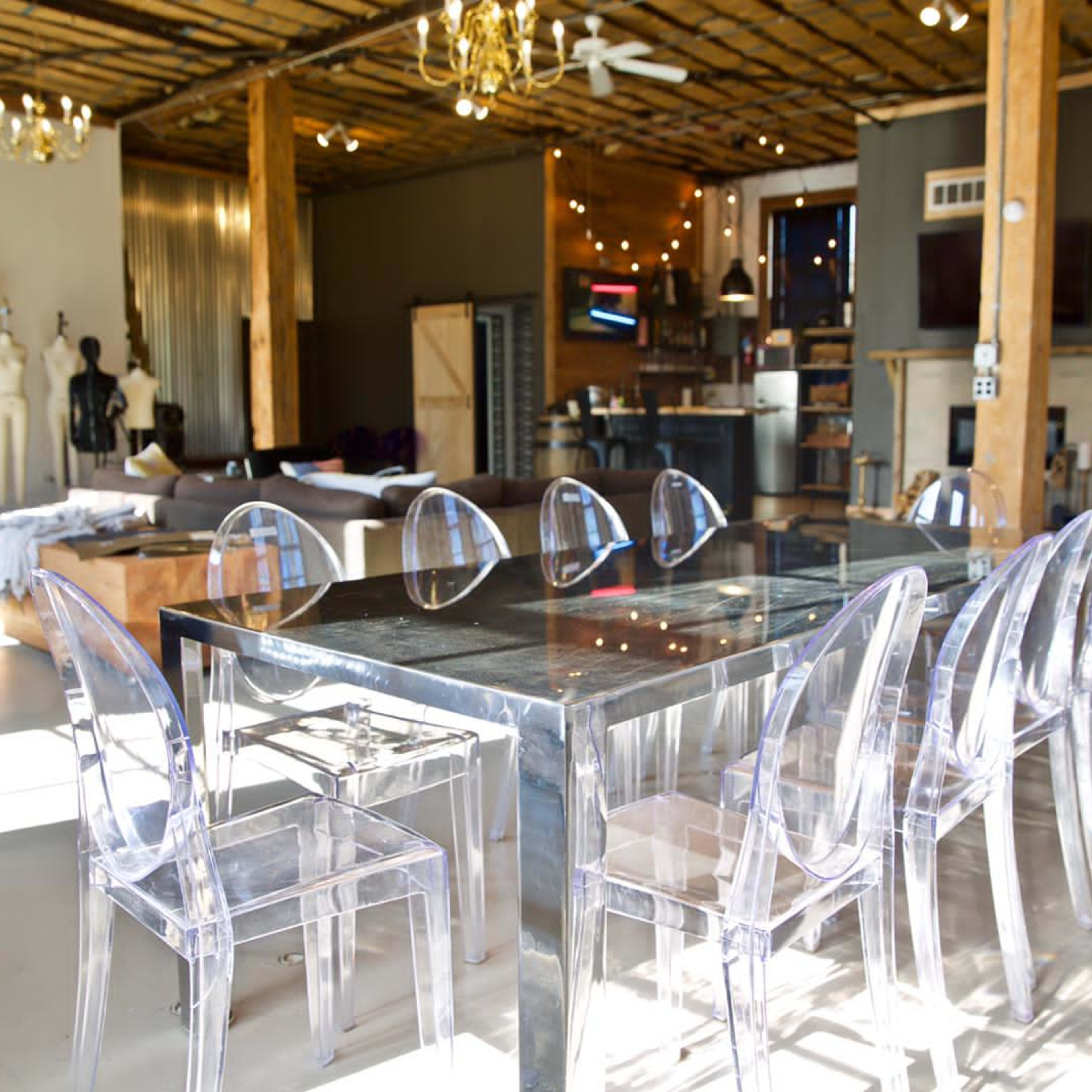 A spacious interior featuring a modern dining table with transparent chairs, wooden beams, and various decorative elements.