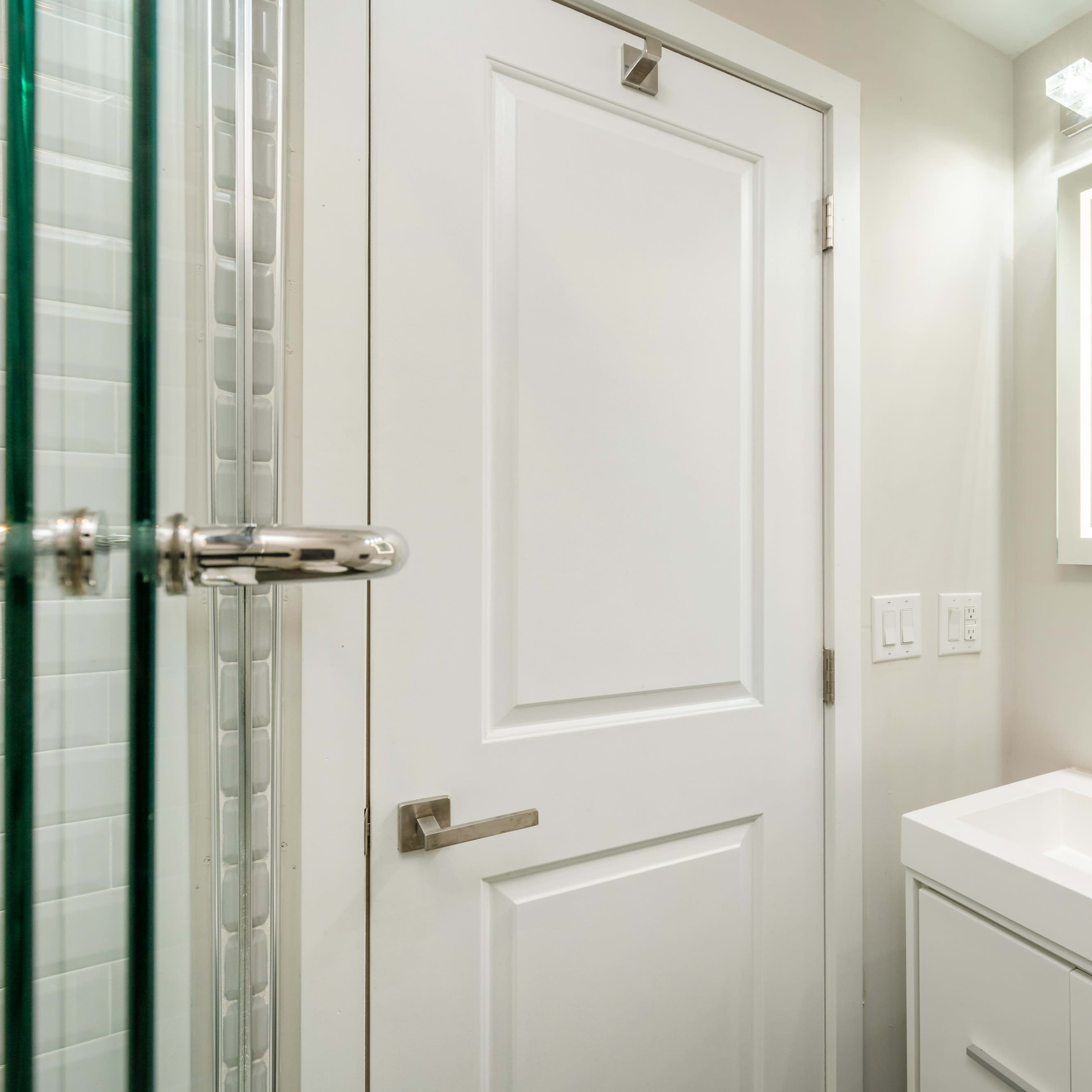 A modern bathroom featuring a white vanity with a sink, a large mirror, and a shower enclosed by glass panels.