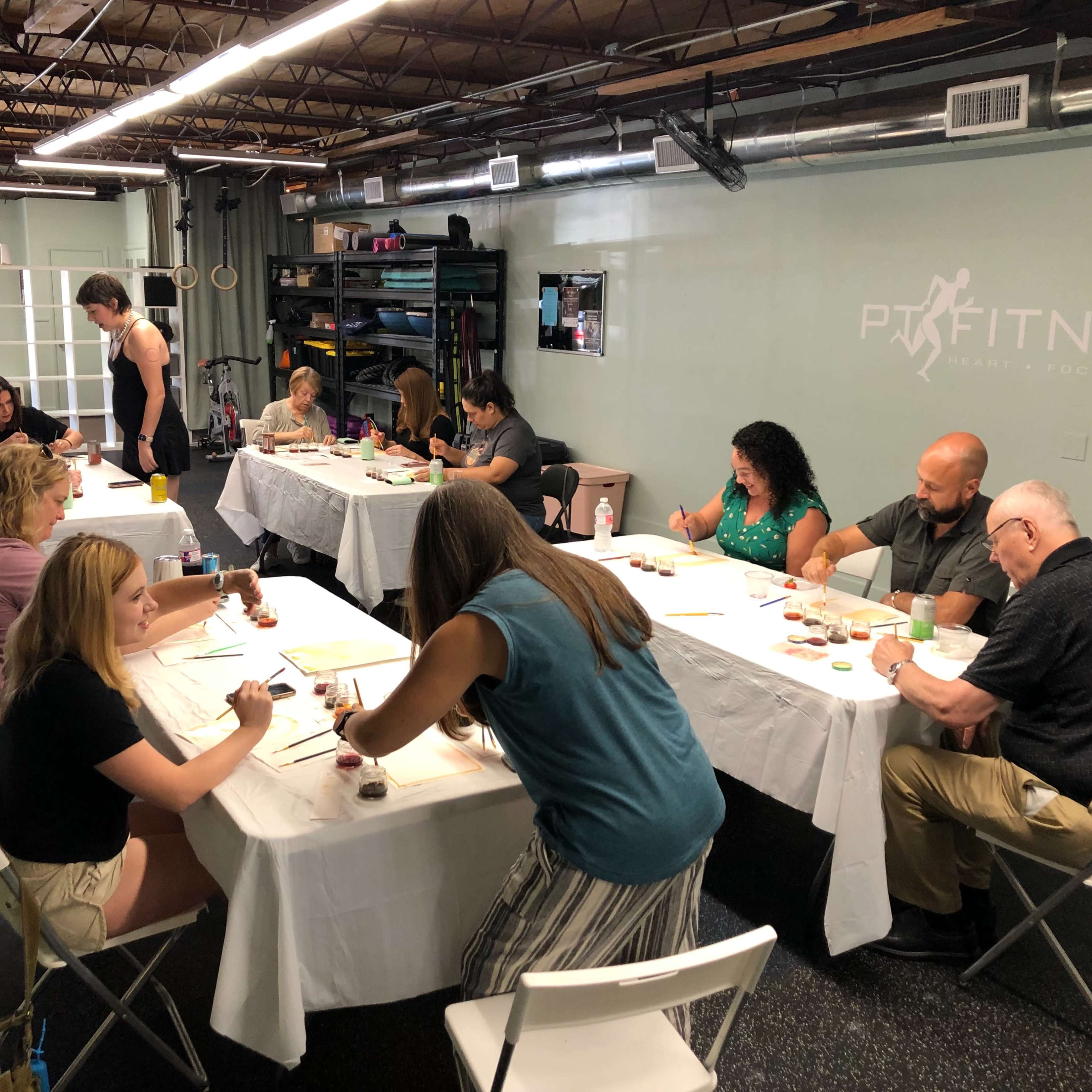 A group of people is engaged in a painting activity at tables in an indoor space.