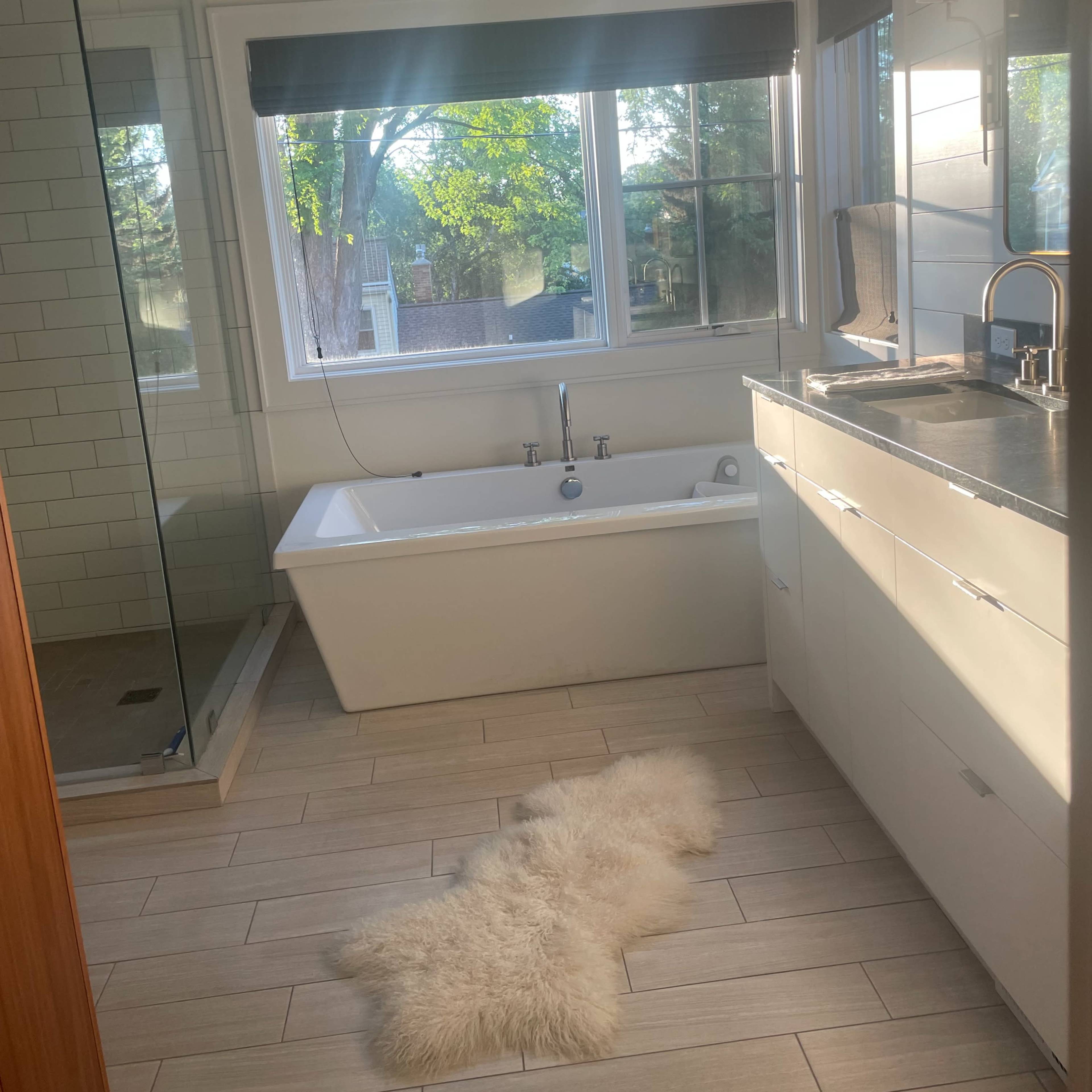 The bathroom features a freestanding tub, a glass shower, and a large window with natural light illuminating the space.