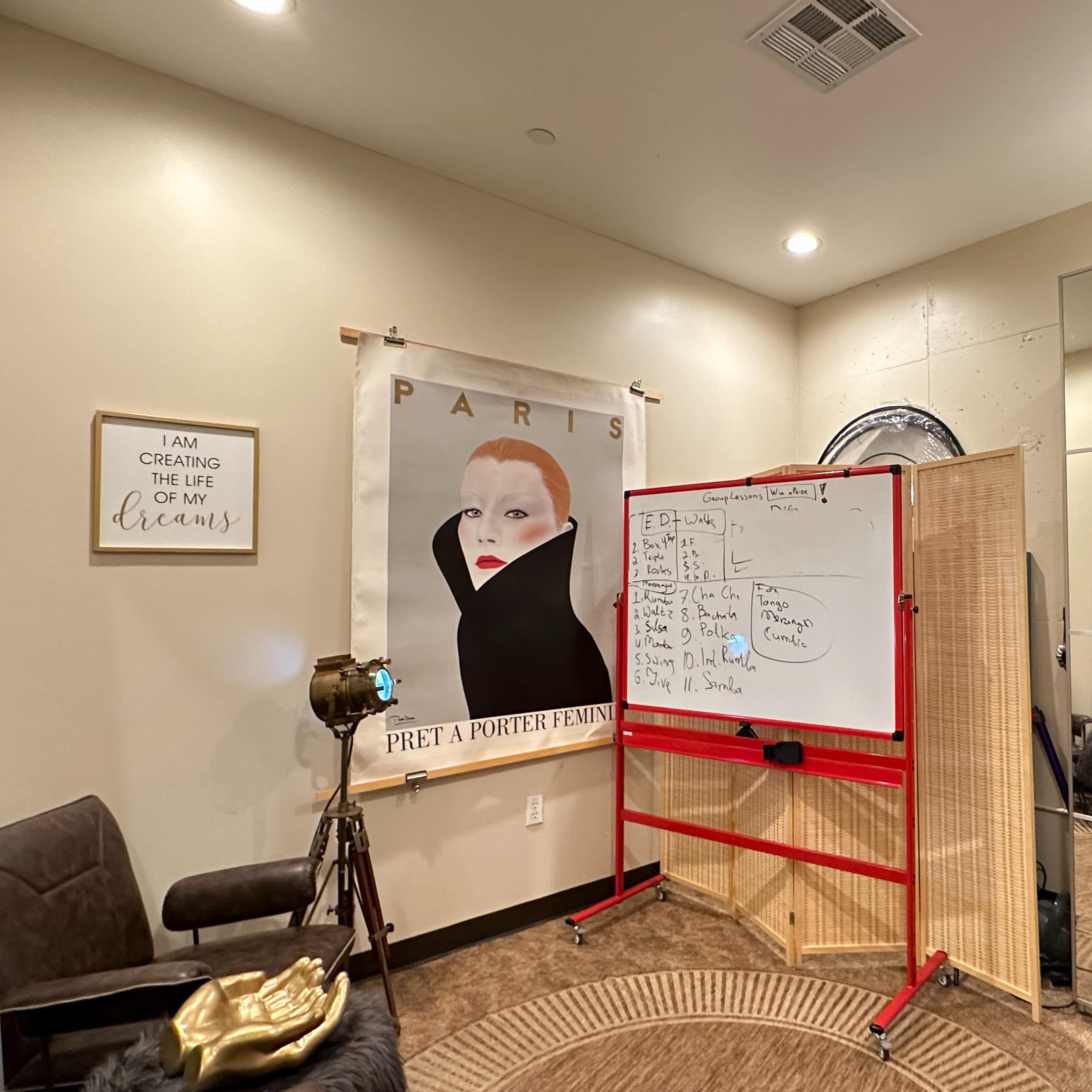 A room features a large poster of a woman in front of a whiteboard, with a partition and furniture arranged for a creative workspace.