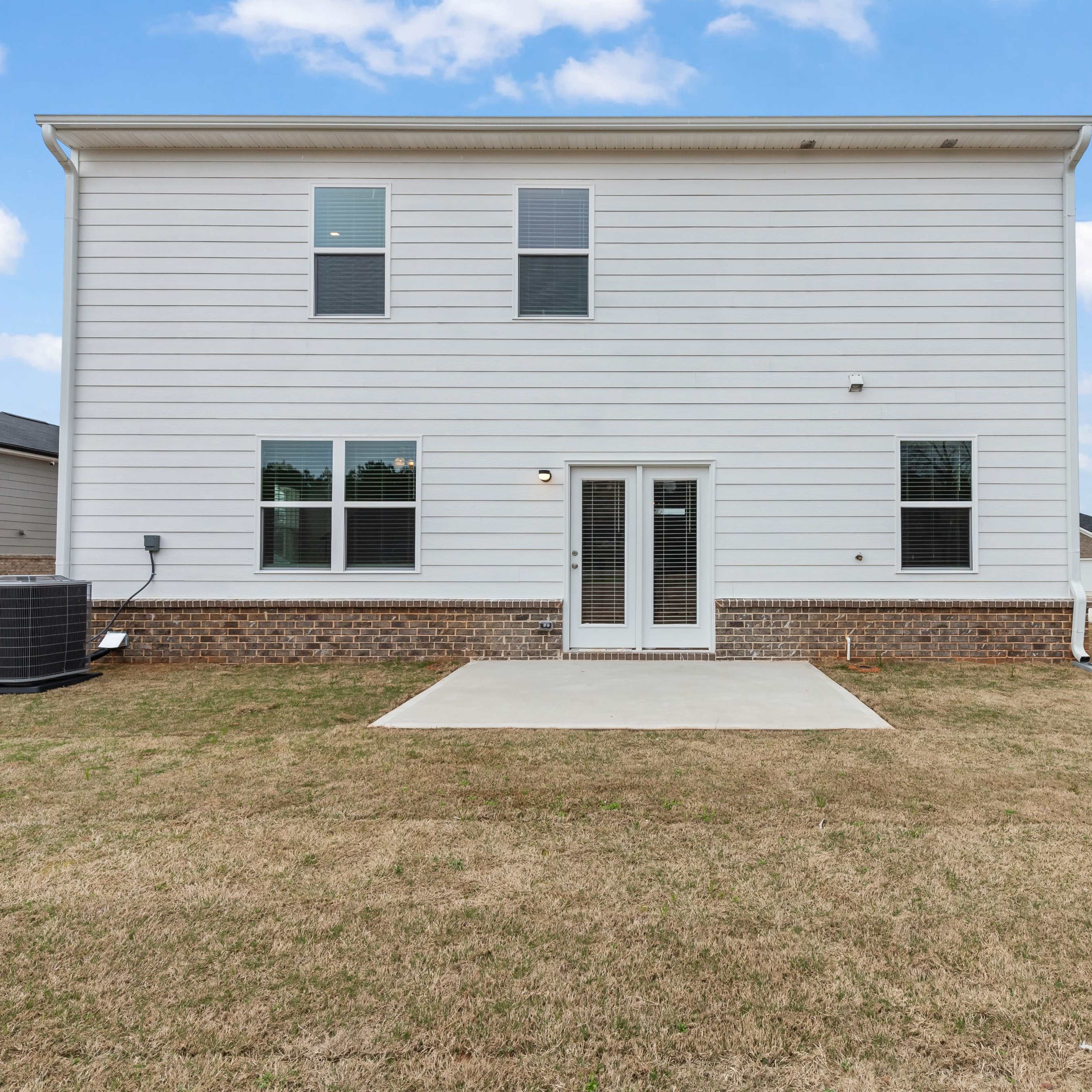 The back view of a two-story house with a concrete patio and grassy backyard.