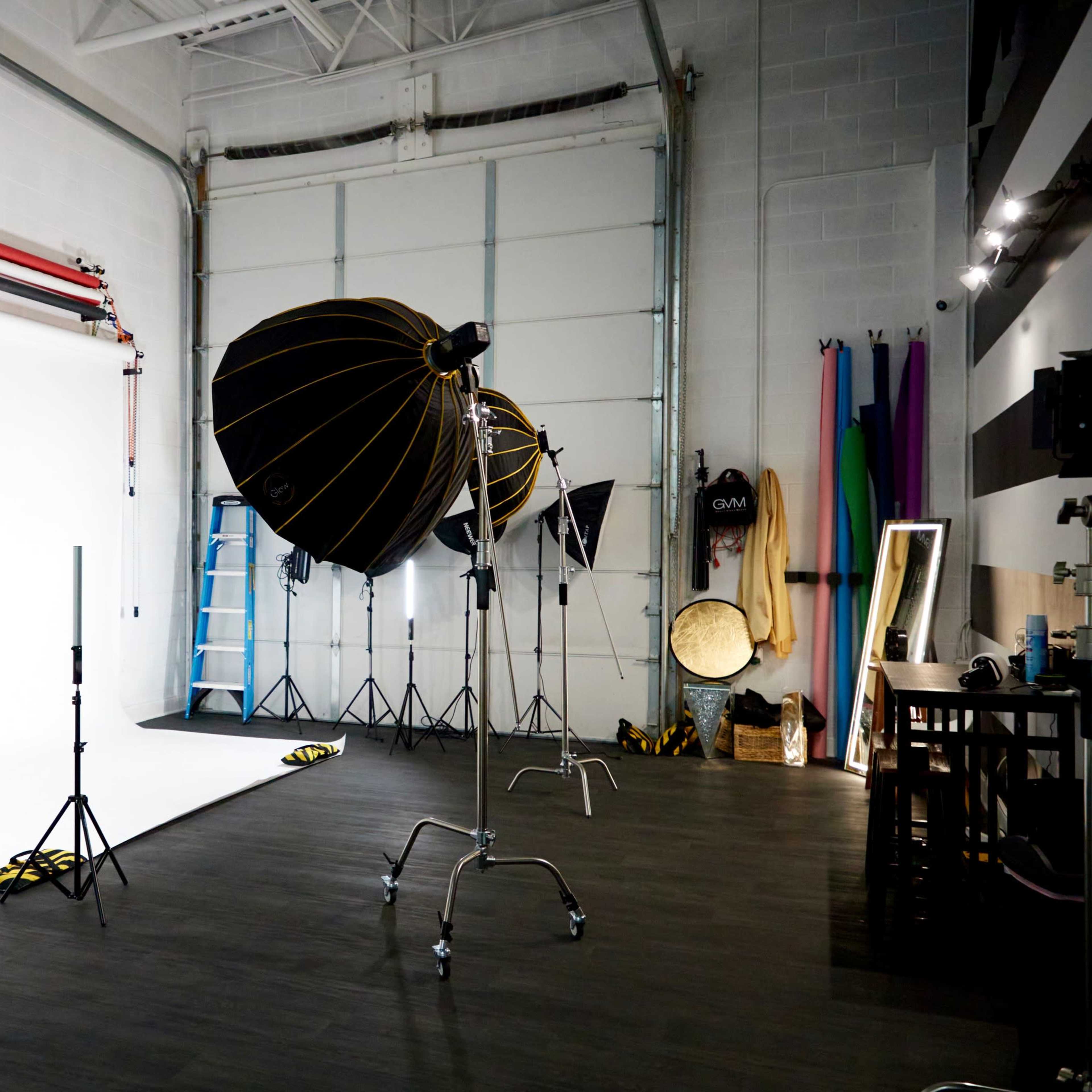 A photography studio equipped with a white backdrop, lighting setups, and various props along the walls.