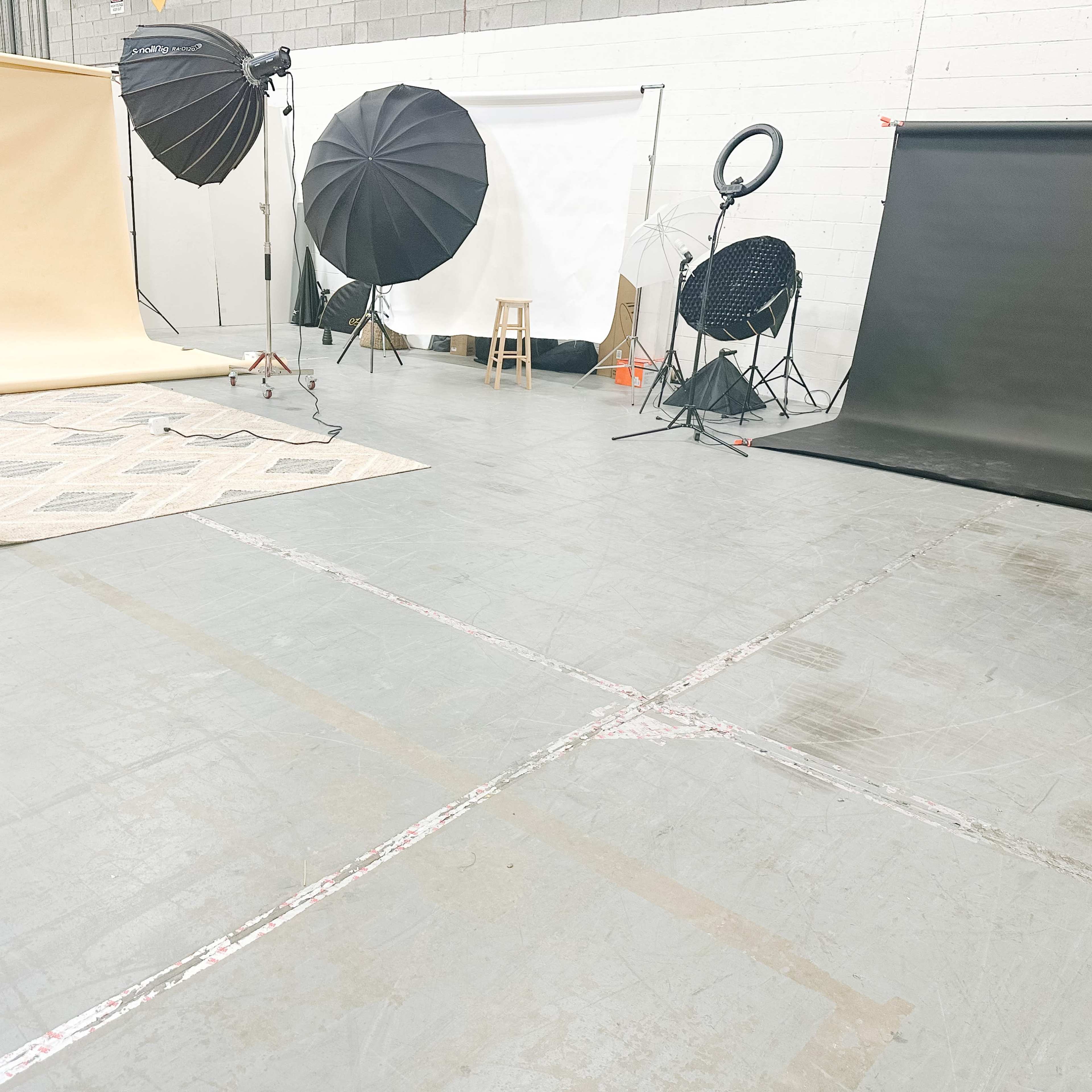 A photography studio setup with various backdrops, lighting equipment, and a chair on a patterned rug.