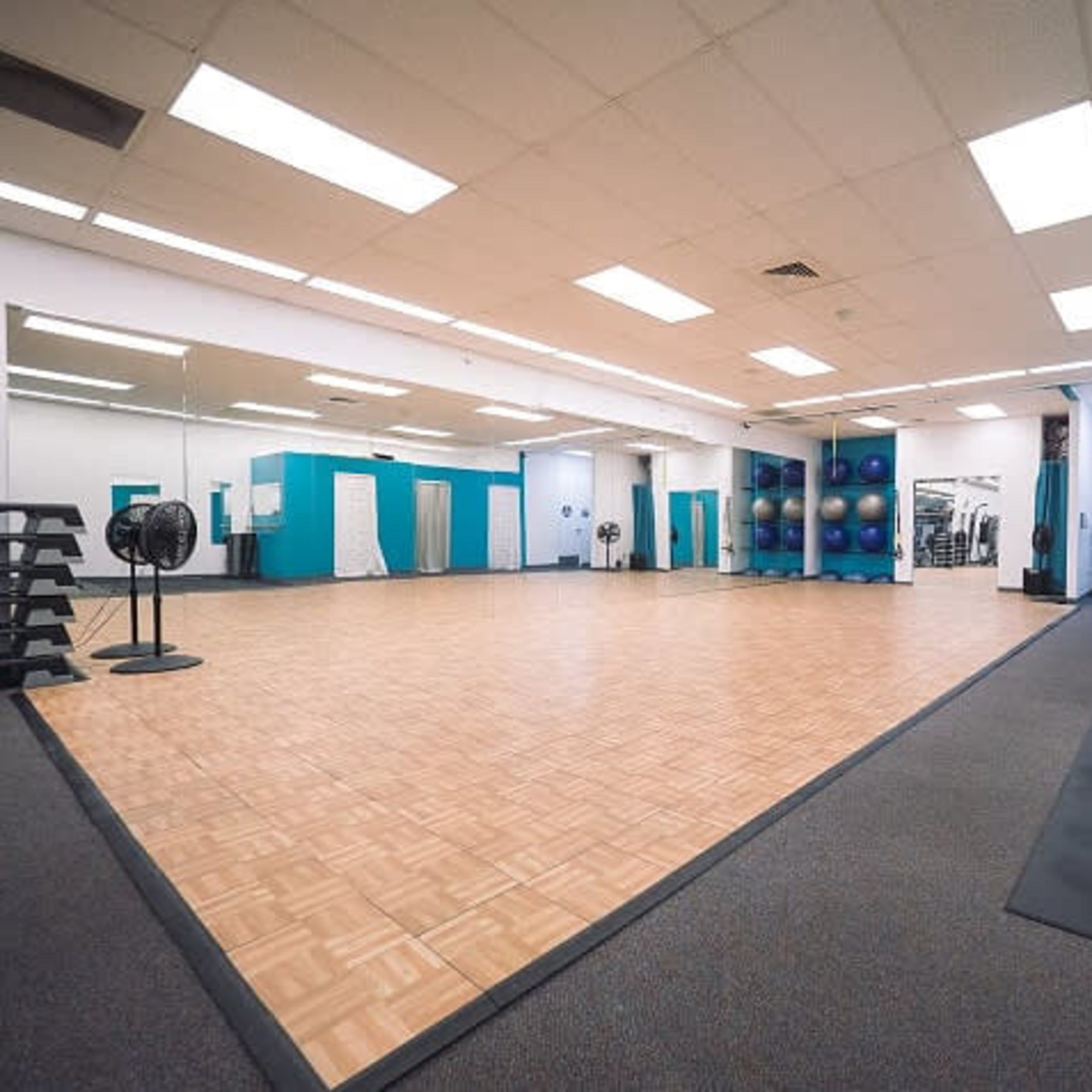 A spacious exercise studio with wooden flooring, mirrors on one wall, and fitness equipment along the side.