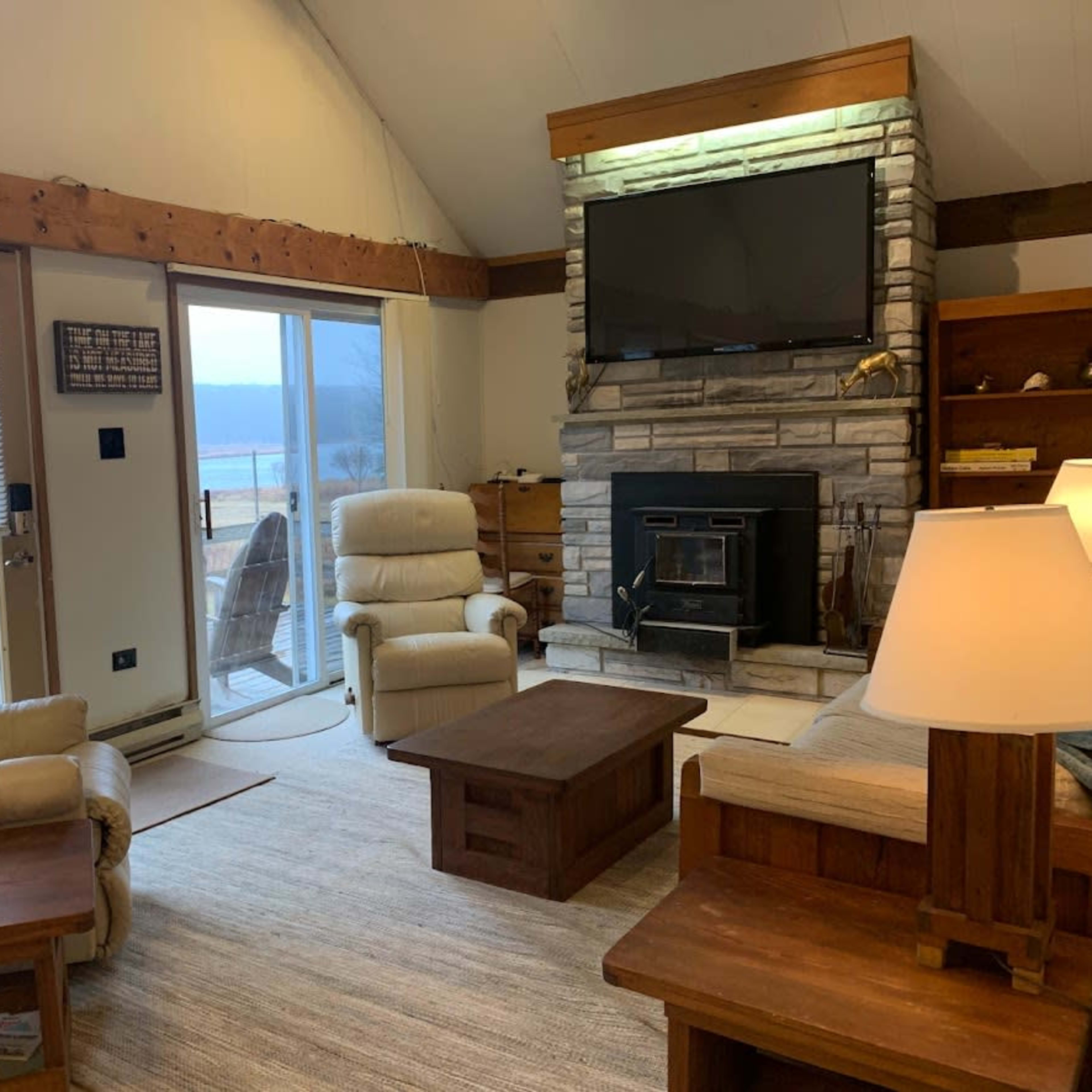 The living room features two reclining chairs, a fireplace with a television above it, and large windows that open to a scenic view.