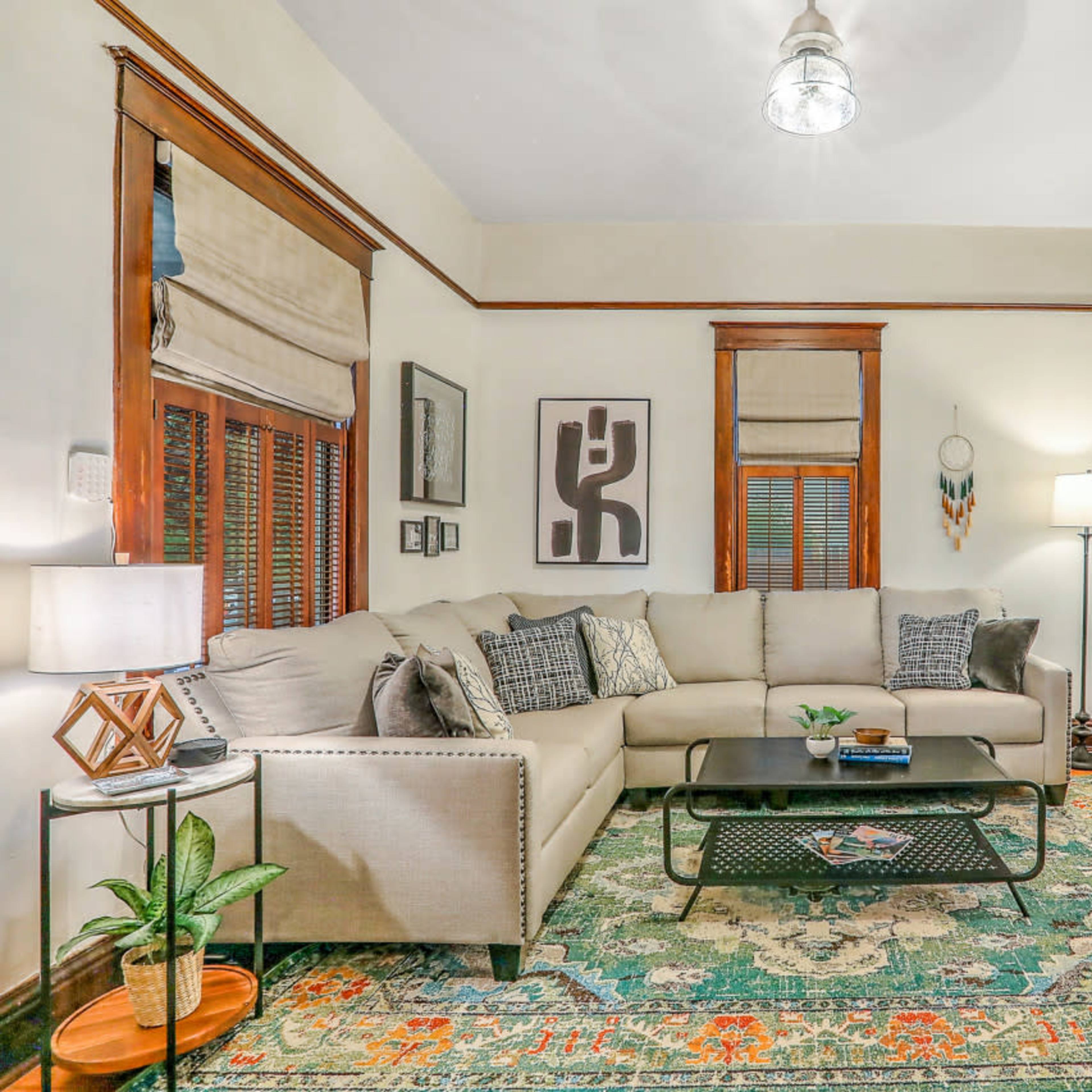 A cozy living room features a sectional sofa, a coffee table, and decorative plants, with warm wooden accents and soft lighting.
