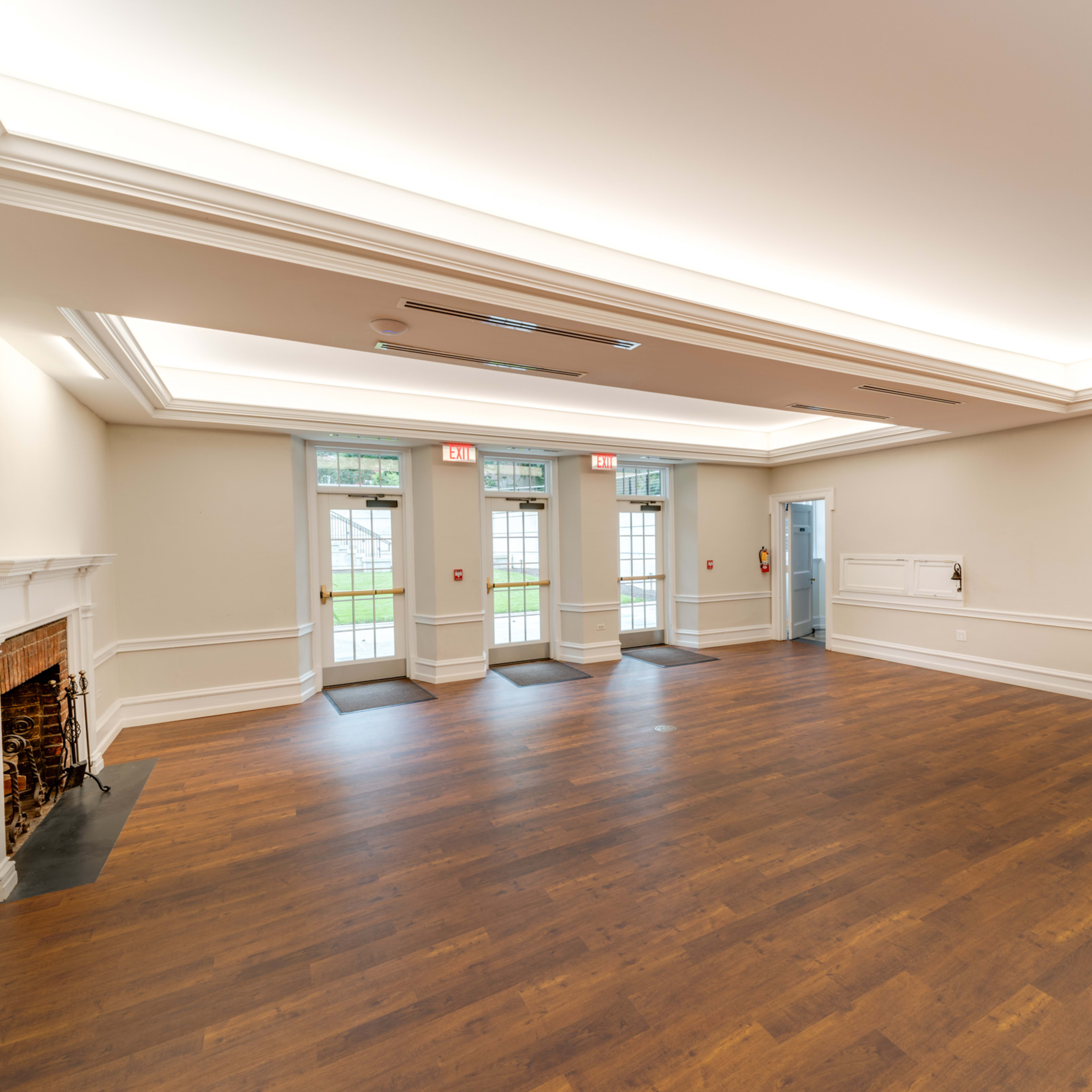 A spacious, empty room with hardwood flooring, large windows, and two sets of double doors leading outside.