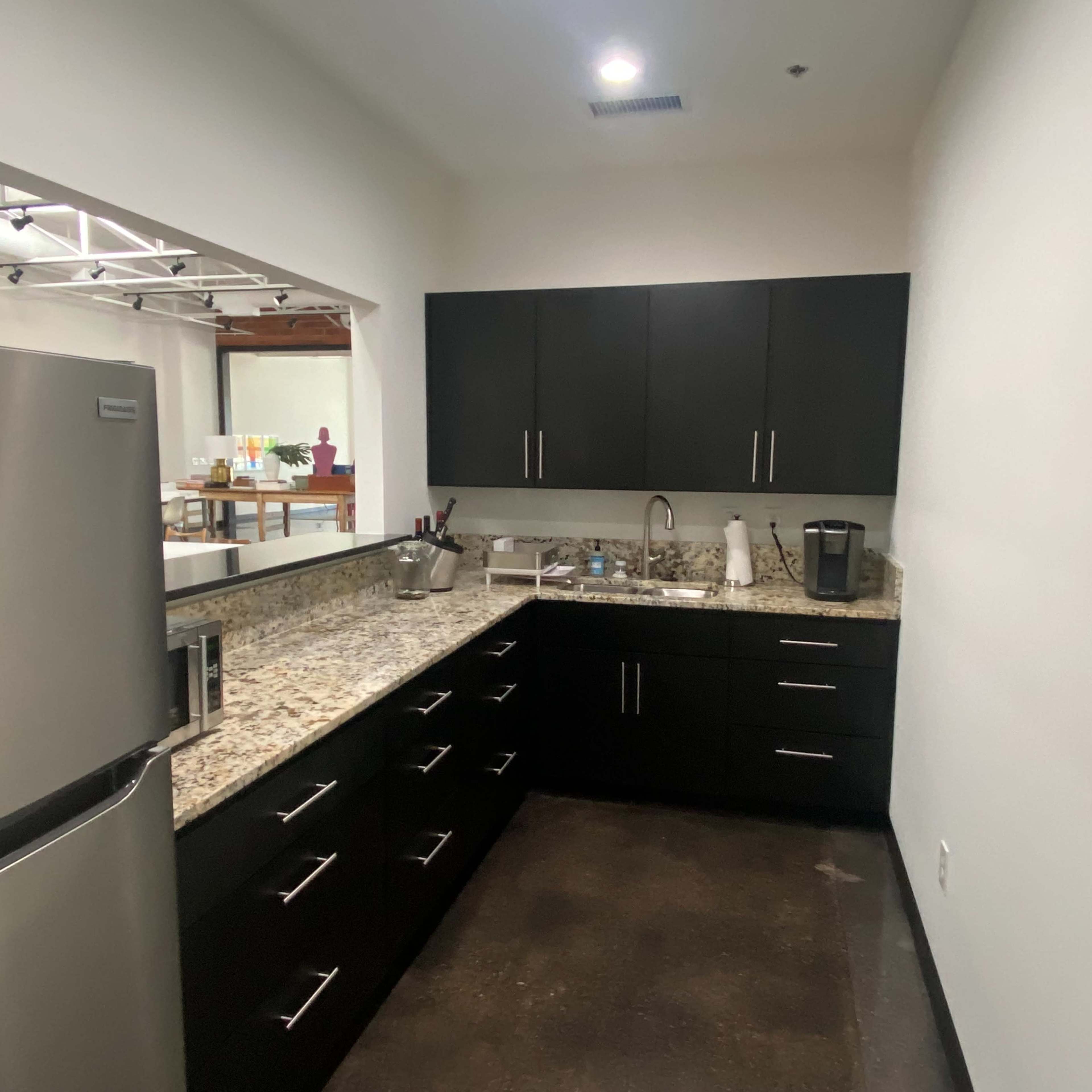A modern kitchen with dark cabinets, a granite countertop, a stainless steel refrigerator, and a coffee maker on the counter.