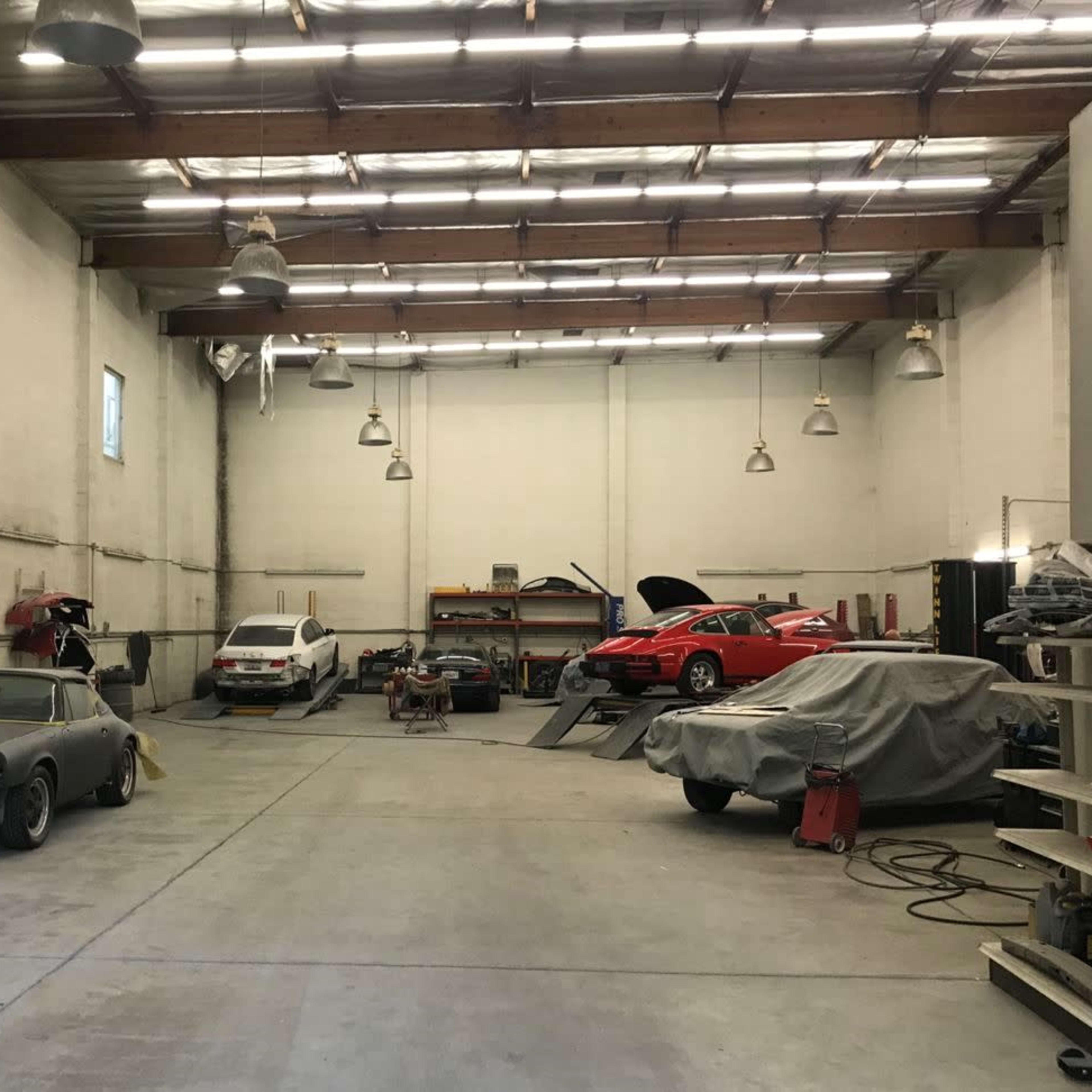 A car workshop features several vehicles, some covered and others being worked on, within a spacious industrial building.