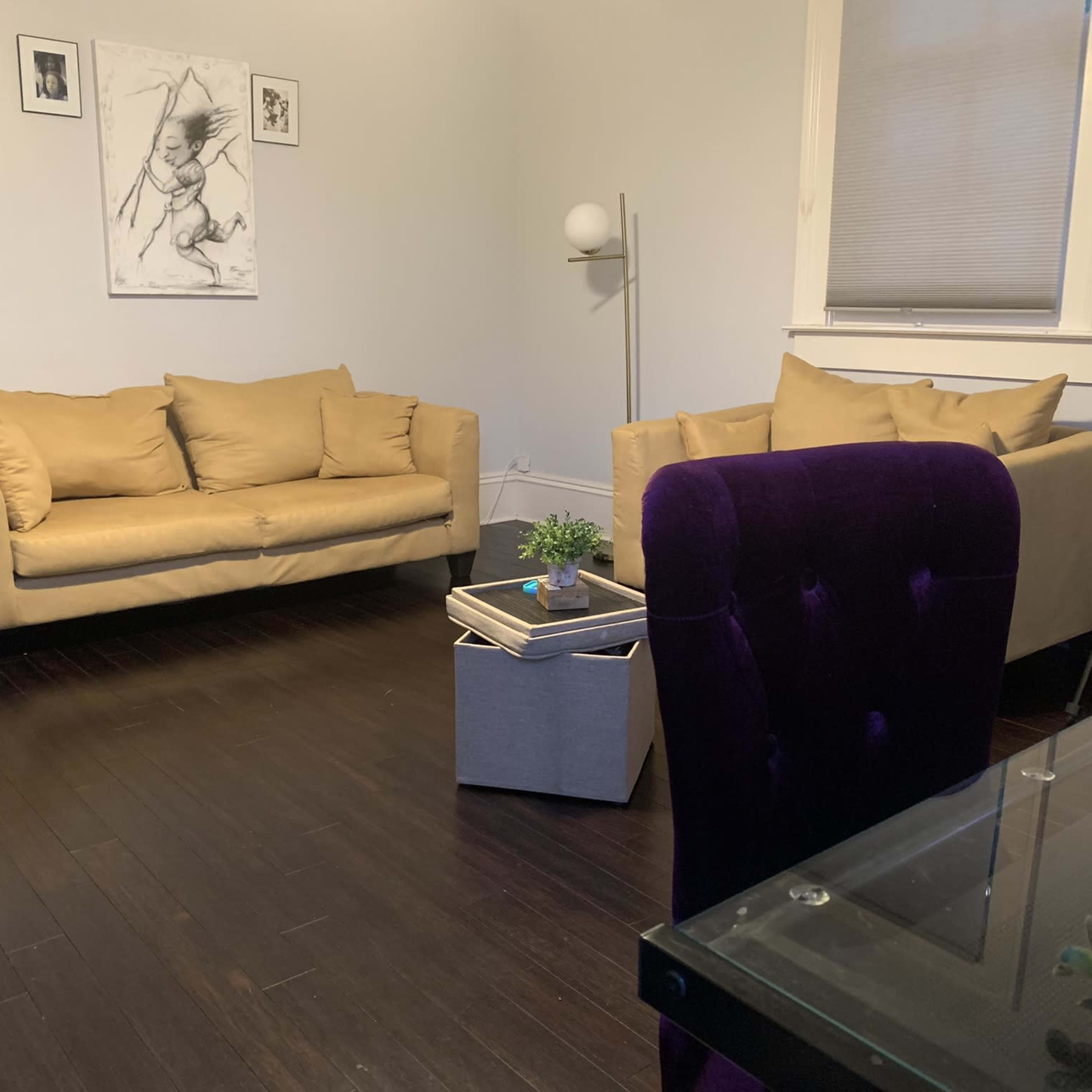 A minimalist living space with two beige sofas facing a small coffee table and a purple chair in front of a glass desk.