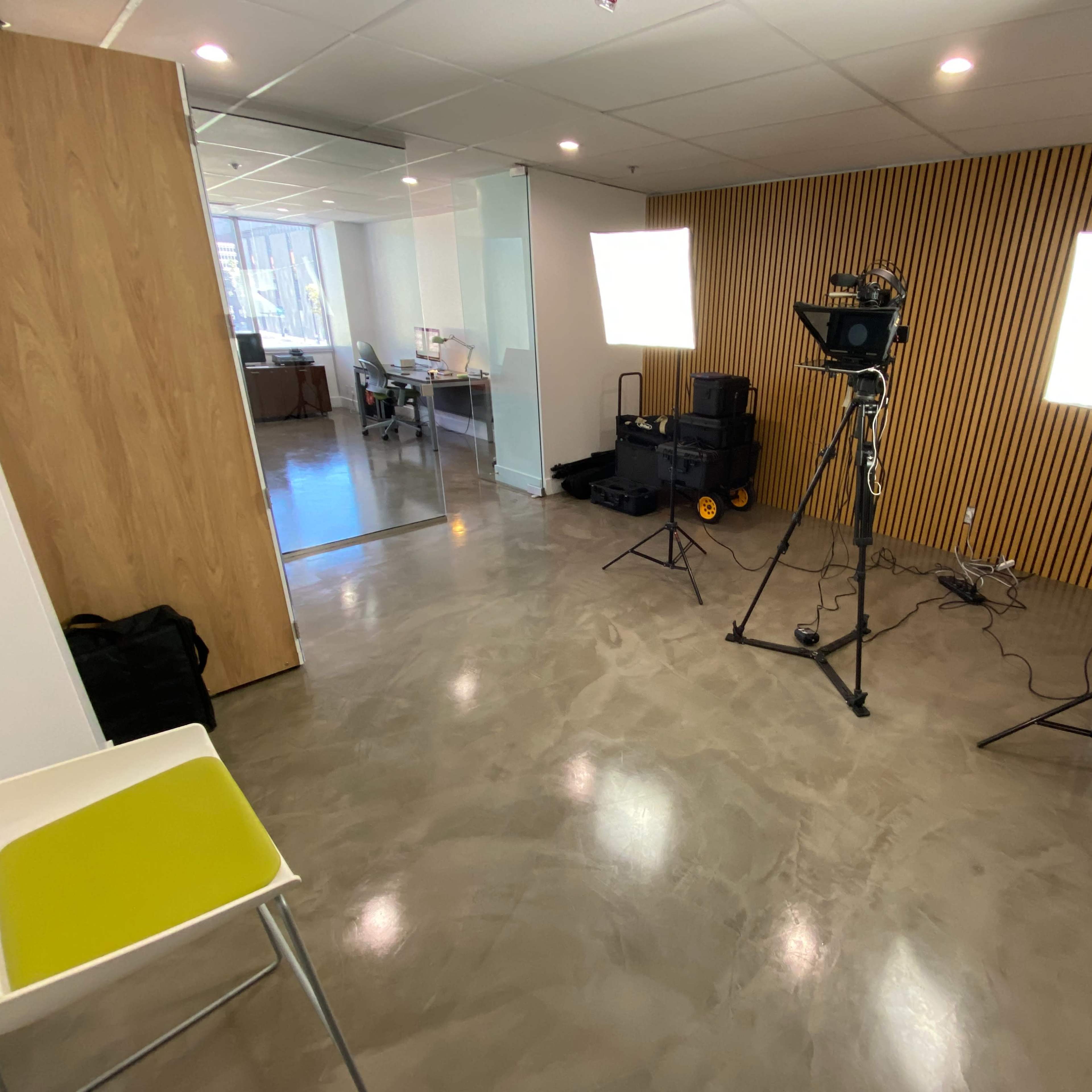 A bright, spacious office setup with studio lighting equipment and a green chair on a polished concrete floor.